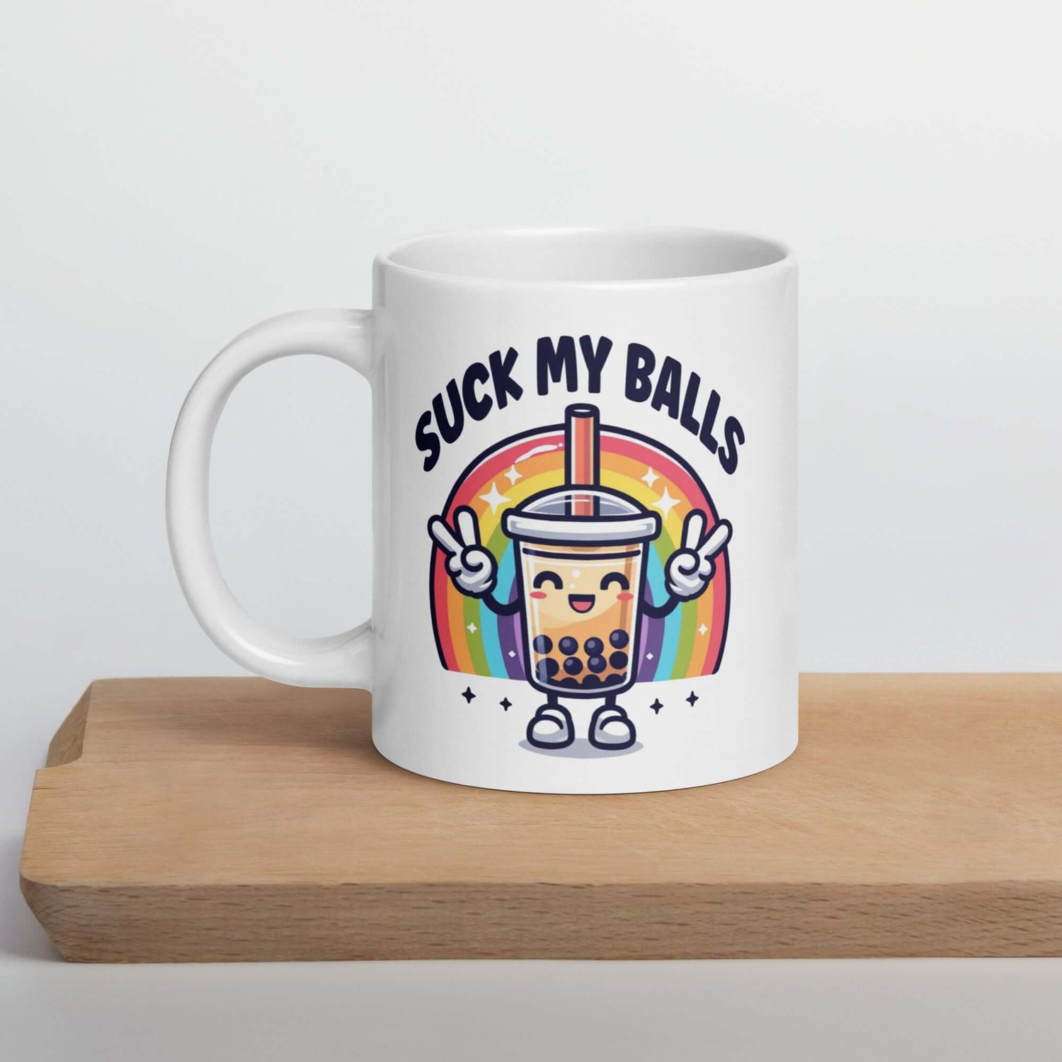 White ceramic mug with graphics of a rainbow and a smiling boba bubble tea. The bubble tea has arms and legs. The phrase Suck my balls is printed above the rainbow. The graphics are on both sides of the mug