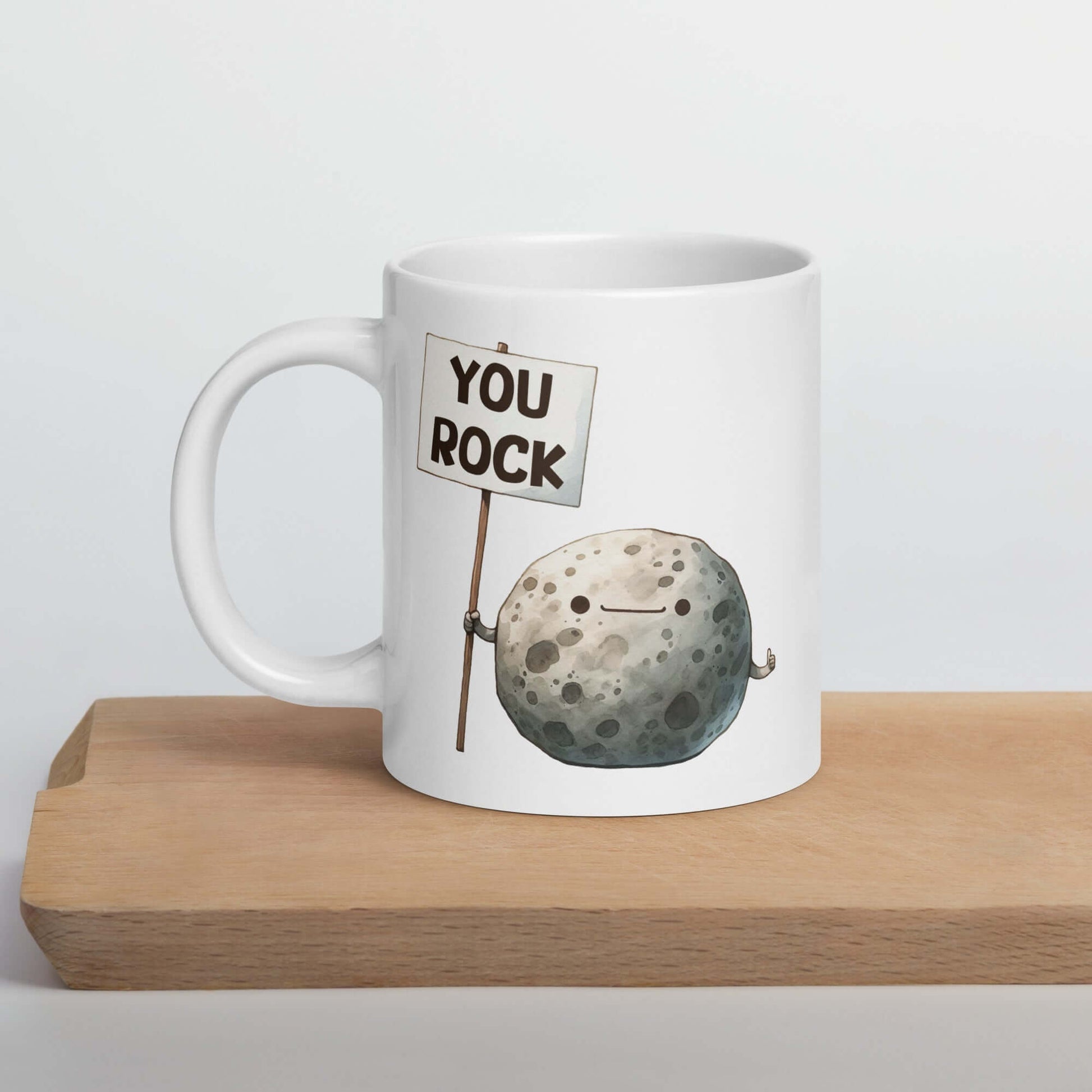 White ceramic mug that has an image of a grey rock that is holding a sign. The sign says You Rock. The image is printed on both sides of the mug.