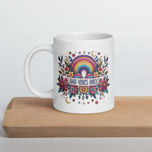 White ceramic mug with a colorful boho rainbow floral design and the phrase Bad Vibes Only printed on both sides of the mug.