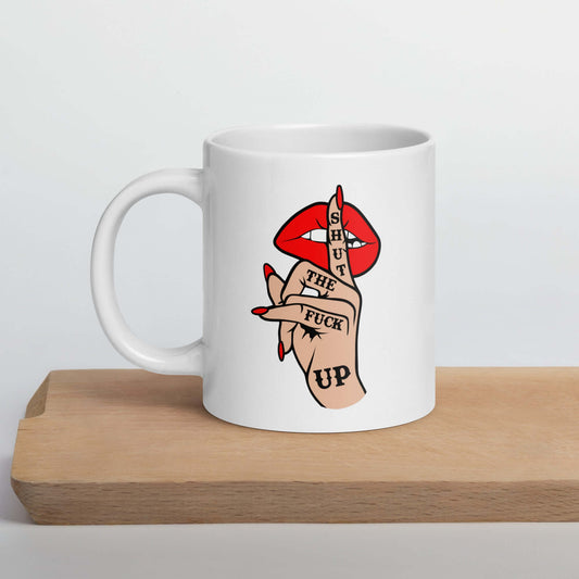 White ceramic mug with an image of a hand over lips making the shh gesture. The words Shut the fuck up are printed on the hand. The graphics are printed on both sides of the mug.