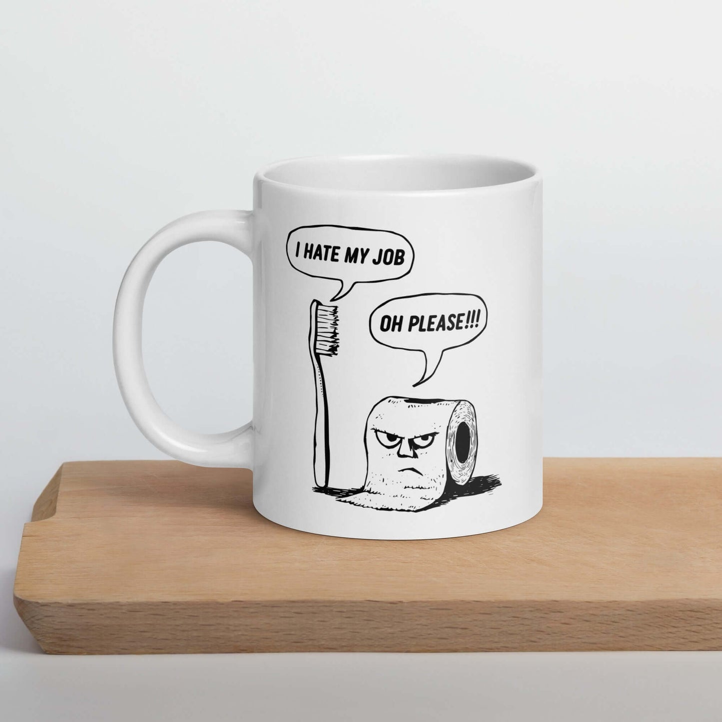 White ceramic mug with a cartoon graphic on both sides. The cartoon is a line drawing of a toothbrush and roll of toilet paper. Both have speech bubbles above . The toothbrush says I hate my job and the toilet paper says Oh please.