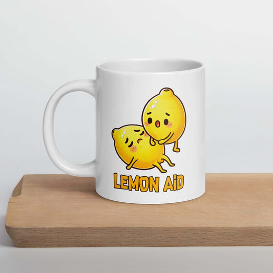 White ceramic mug with image of 2 cartoon lemons. One lemon is giving the other lemon CPR. The words Lemon Aid is under the lemons. The graphics are printed on both sides of mug.