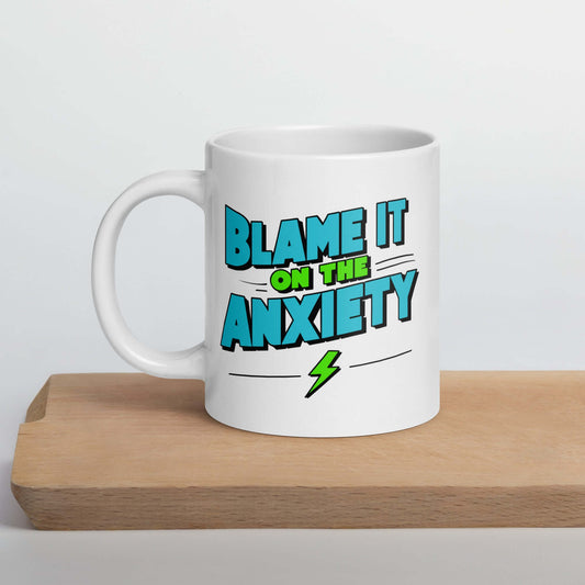 White ceramic mug with the phrase Blame is on the anxiety printed on both sides. The graphics are bold and in aqua and lime green.