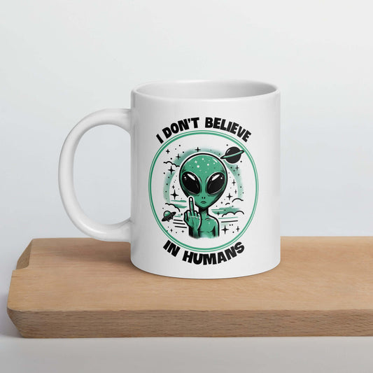 White ceramic mug with an image of an alien flipping the middle finger. The words I don't believe in humans are printed around the image. The graphics are printed on both sides of the mug.