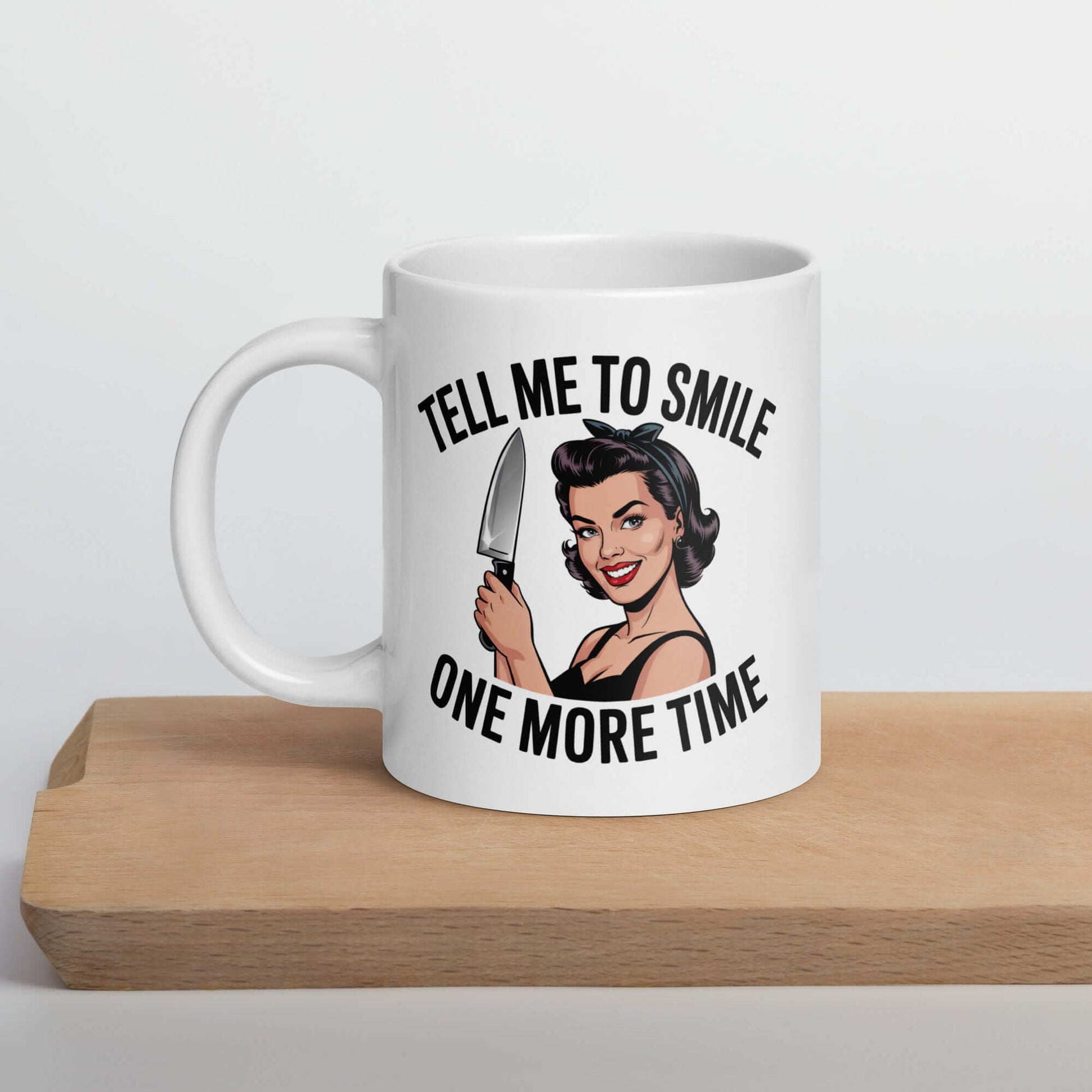 White ceramic mug with graphic of a woman holding a knife and the phrase 'Tell me to smile one more time'. 