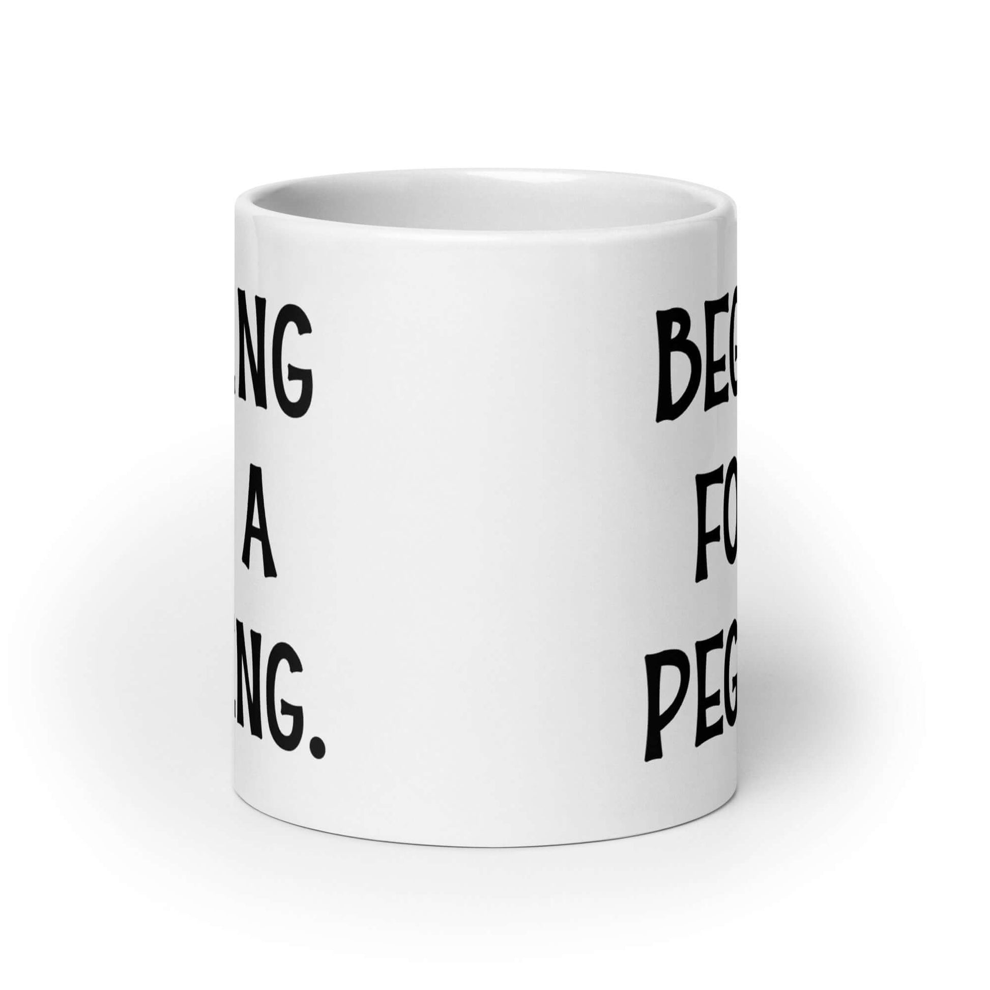 White ceramic coffee mug with the words Begging for a pegging printed on both sides.