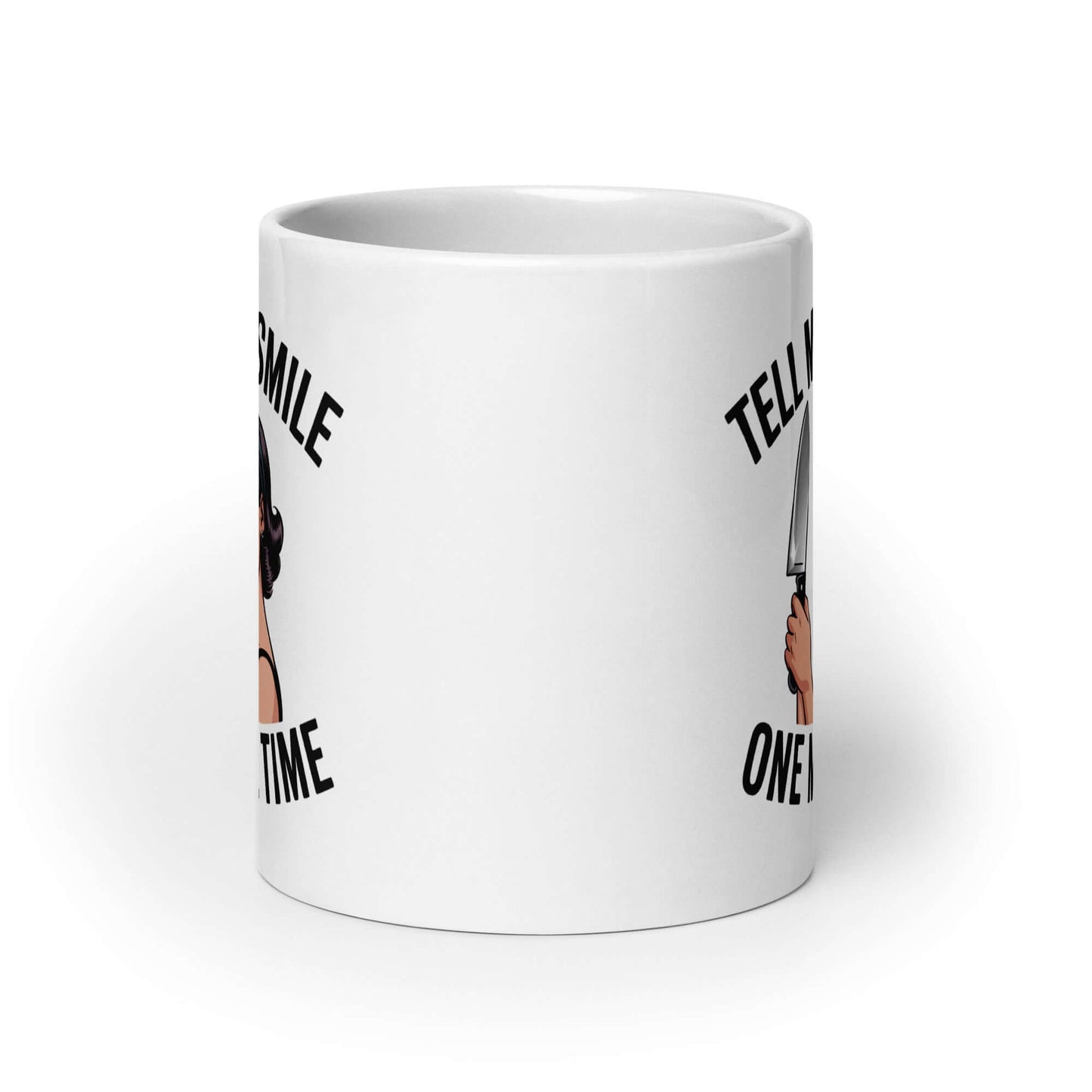 White ceramic mug with graphic of a woman holding a knife and the phrase 'Tell me to smile one more time'. 