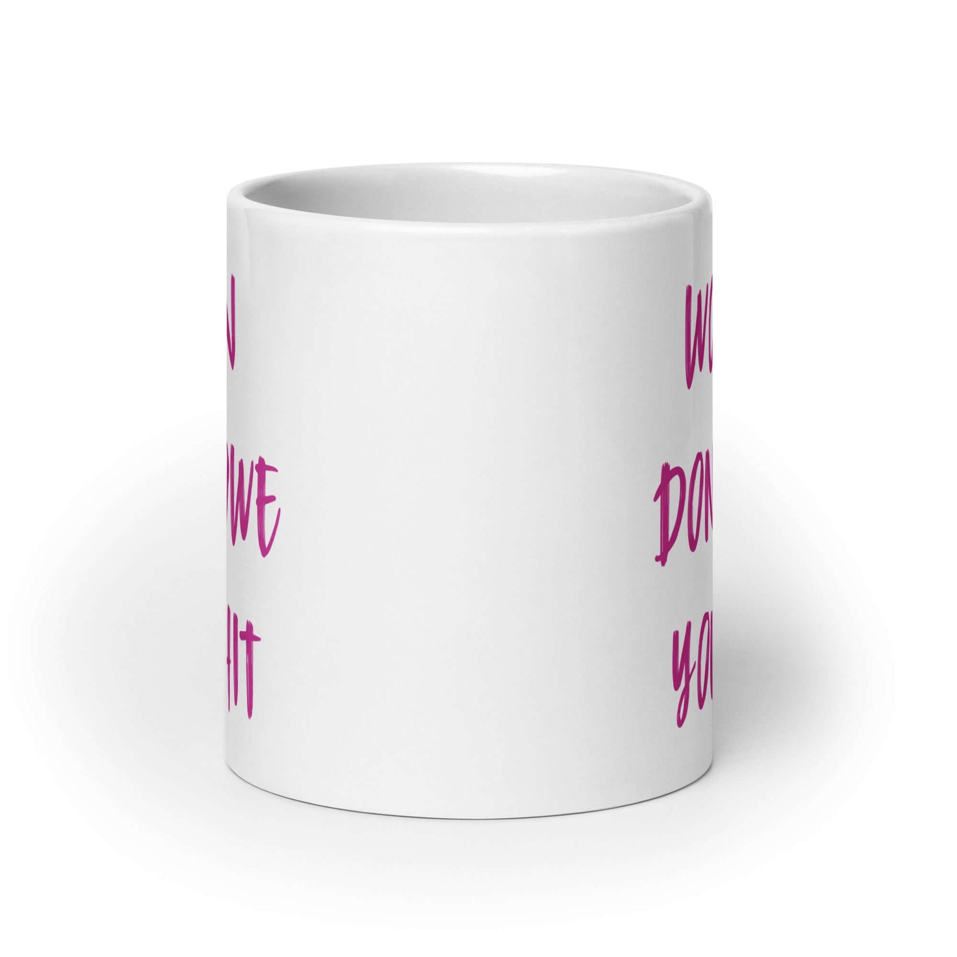 White ceramic coffee mug with the words Women don't owe you shit printed on both sides in pink.