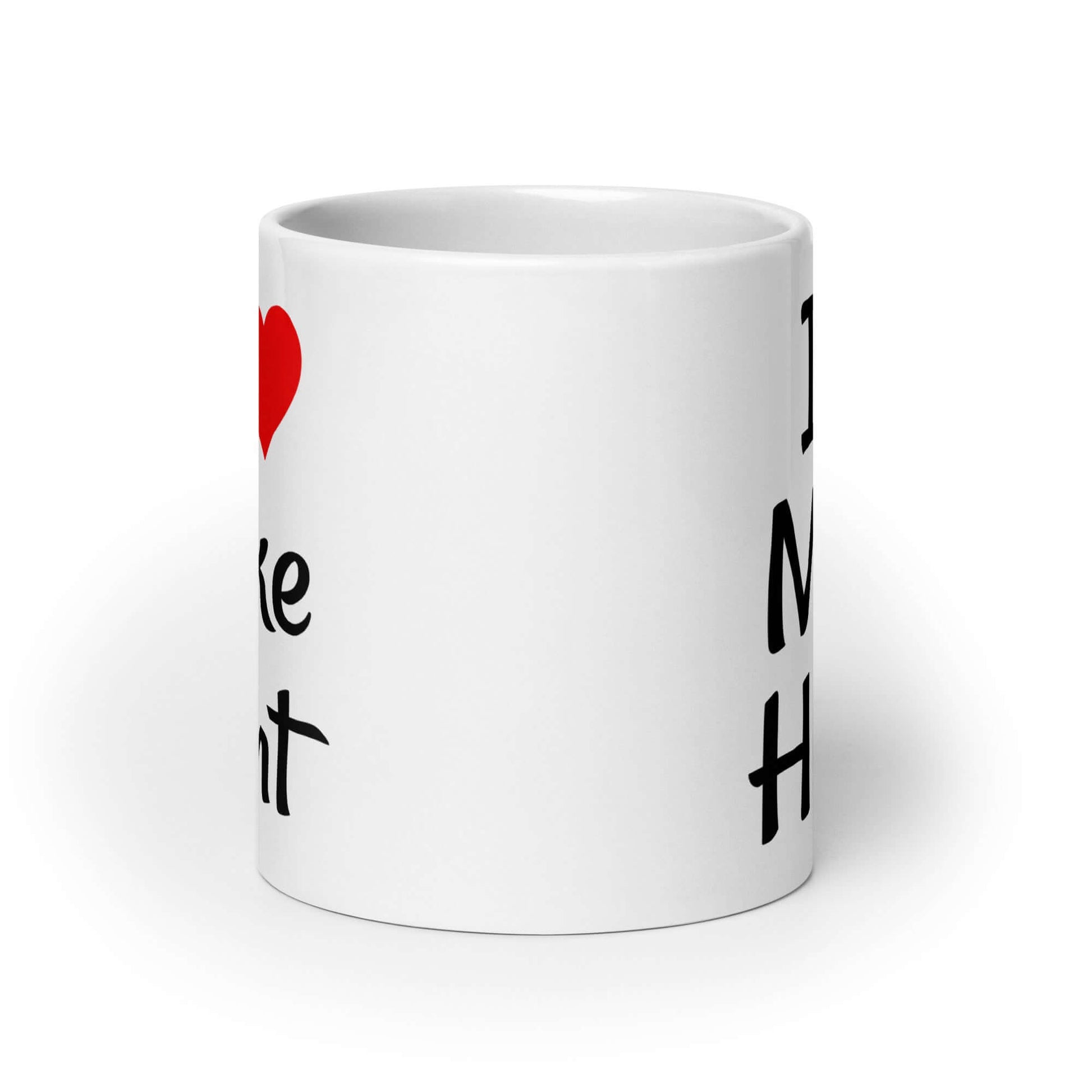 White ceramic coffee mug with pun I heart Mike Hunt printed on both sides of the mug. The heart is red.