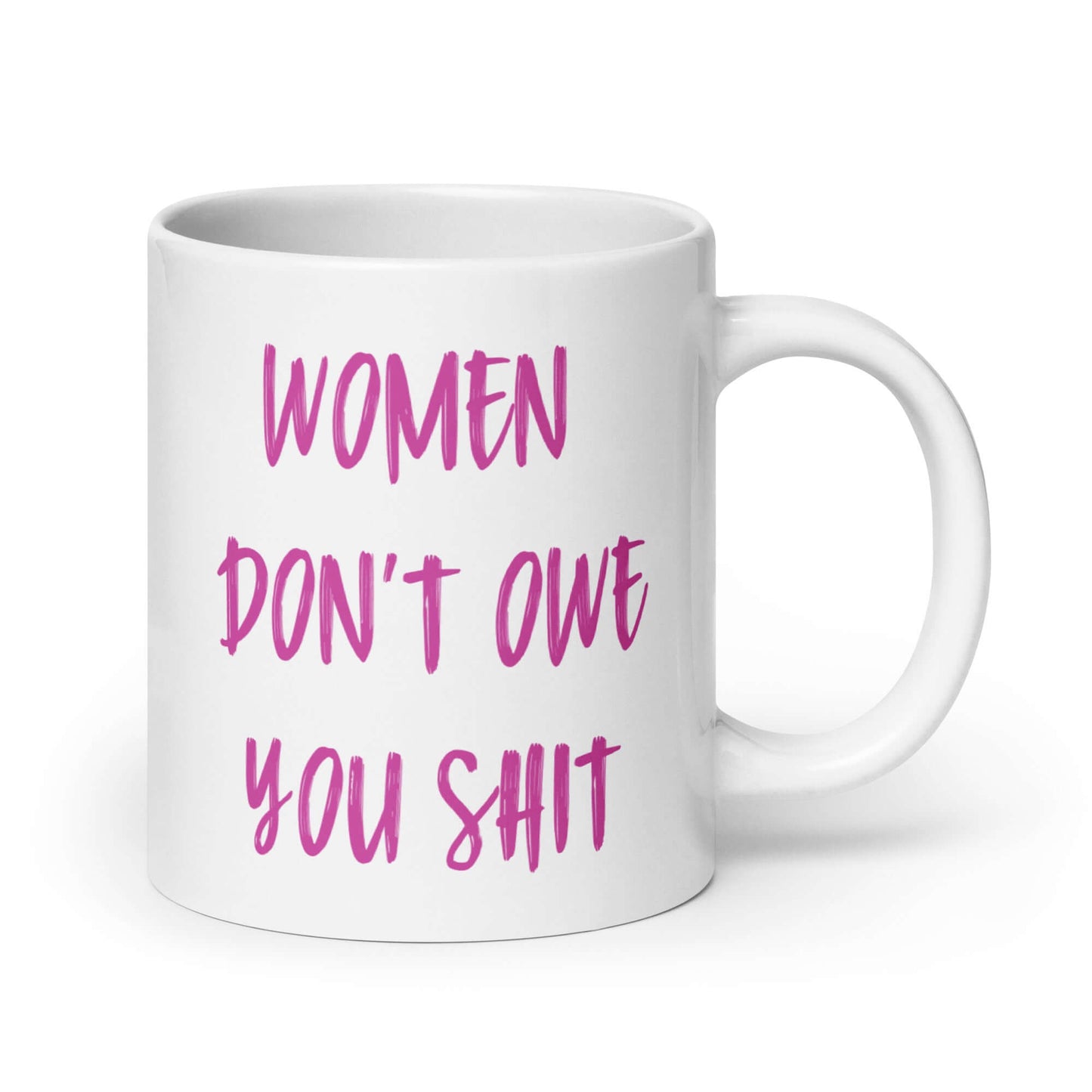 White ceramic coffee mug with the words Women don't owe you shit printed on both sides in pink.