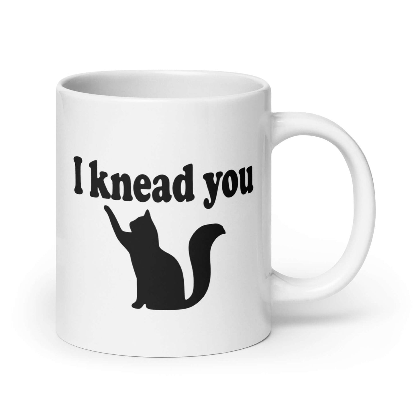 White ceramic coffee mug that has a pun image of a silhouette of a cat and the words I knead you printed on both sides of the mug.
