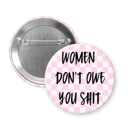 Button badge with 'Women Don't Owe You Shit' text on a pink checkered background