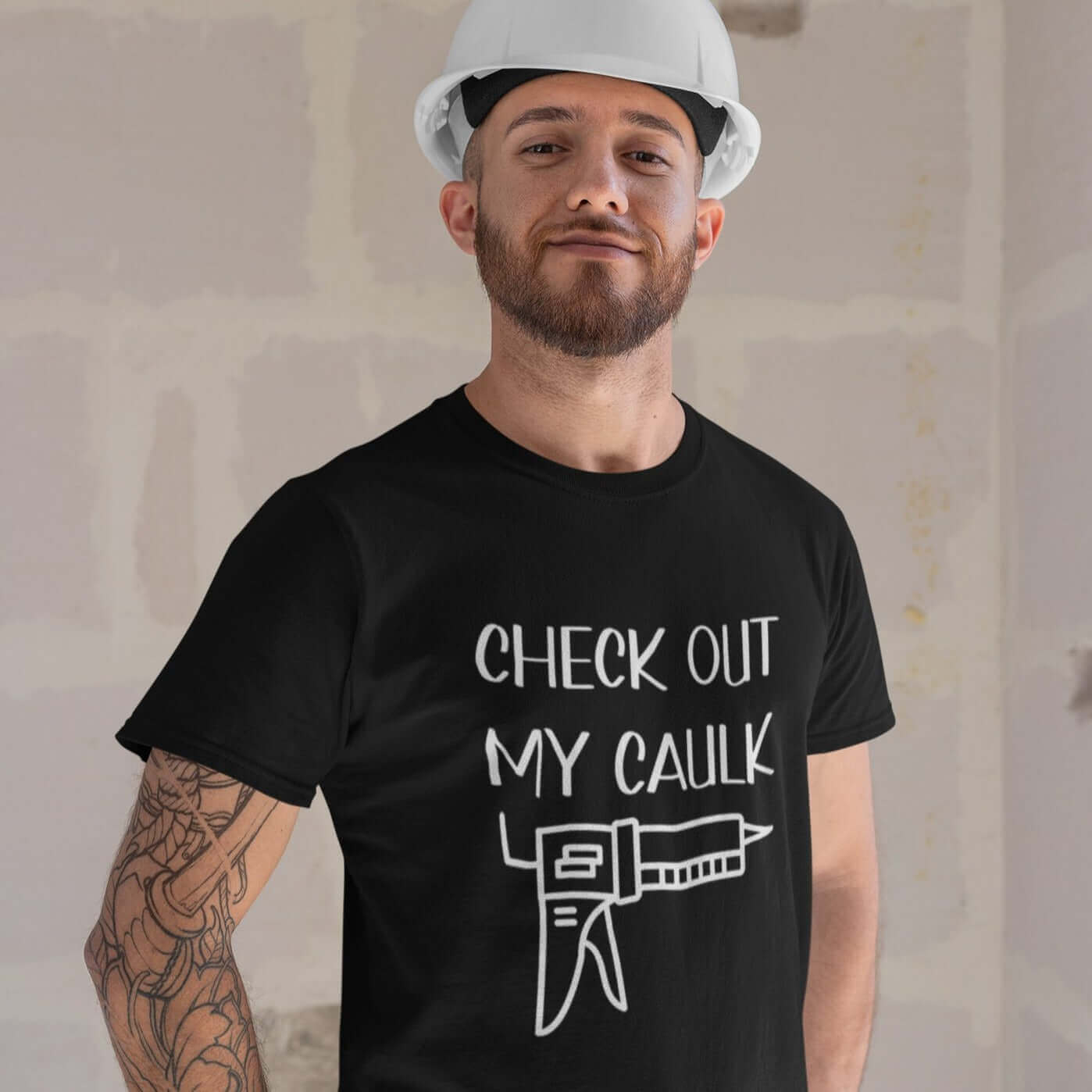 Man wearing a hardhat and a black t-shirt with the pun phrase Check out my caulk with a line drawing image of a caulking gun printed on the front.