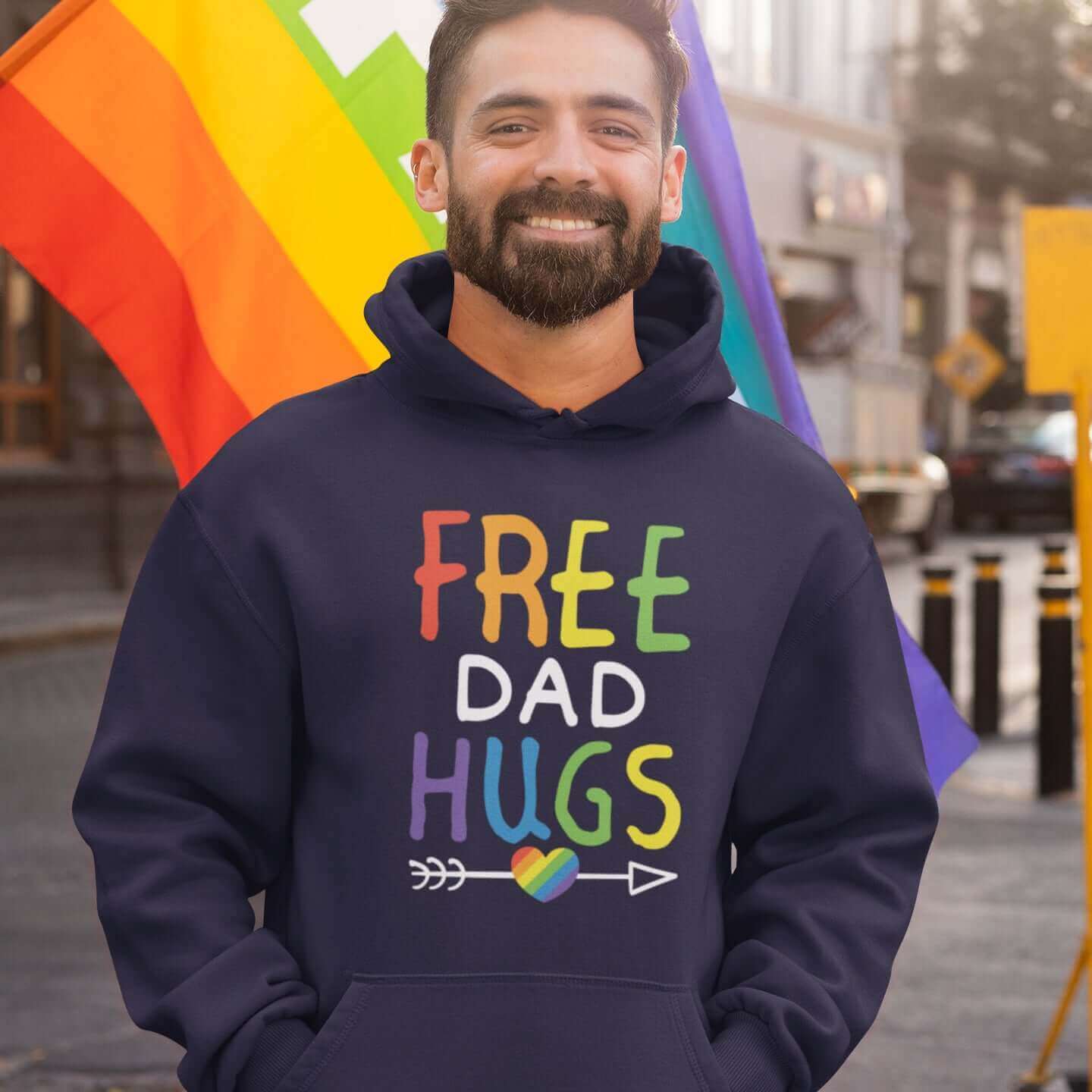 Man at gay pride event wearing navy blue hoodie sweatshirt with the words Free Dad hugs printed on the front in rainbow letters.