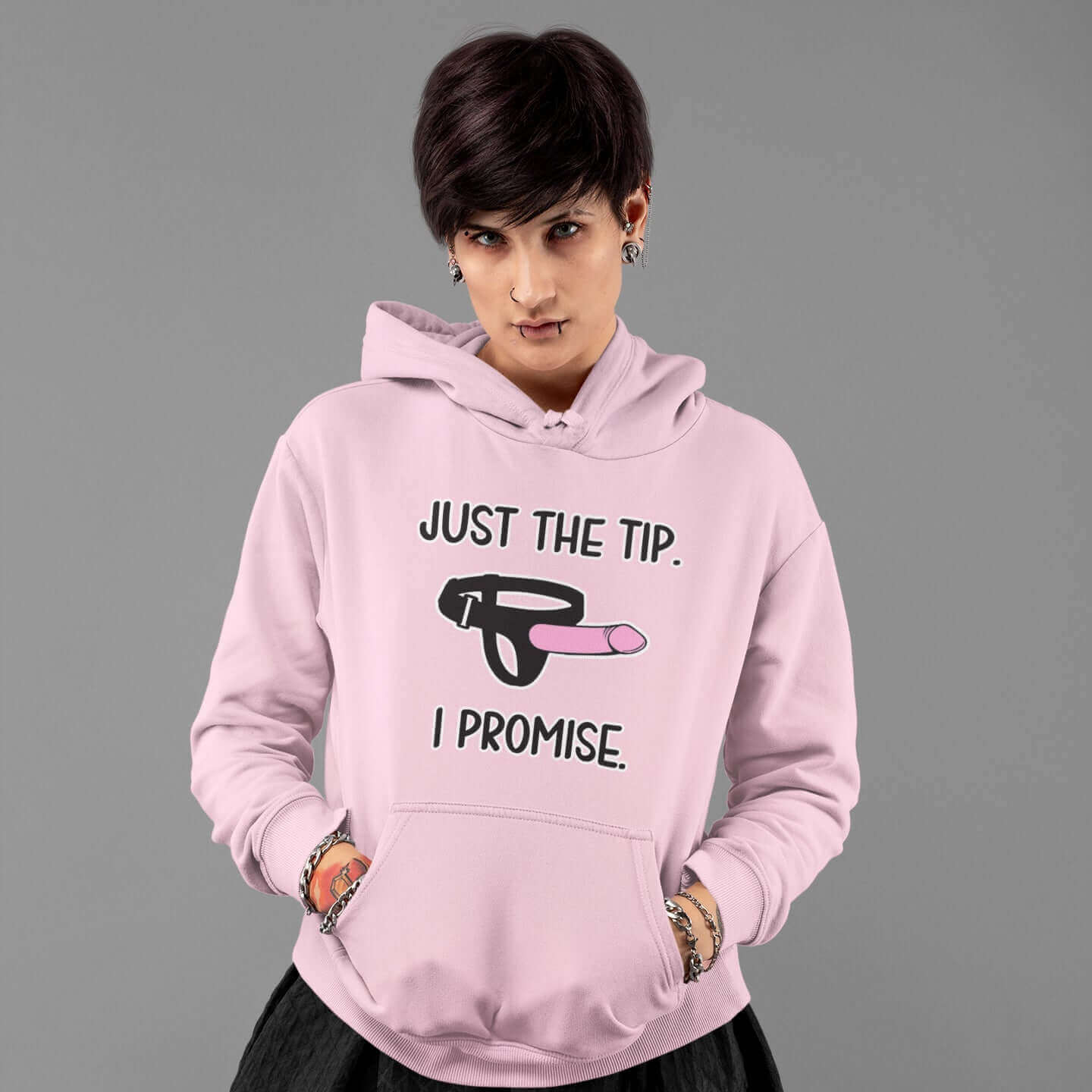 Alternative looking woman with shirt hair wearing a light pink hoodie sweatshirt. The hoodie has an image of a strap-on dildo and the words Just the tip, I promise printed on the front.