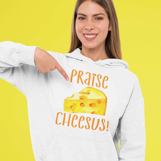 Woman wearing white hoodie sweatshirt pointing at the graphic on her hoodie. The graphics are of a piece of swiss cheese and the words Praise Cheesus printed on the front of the hoodie in yellow and orange.