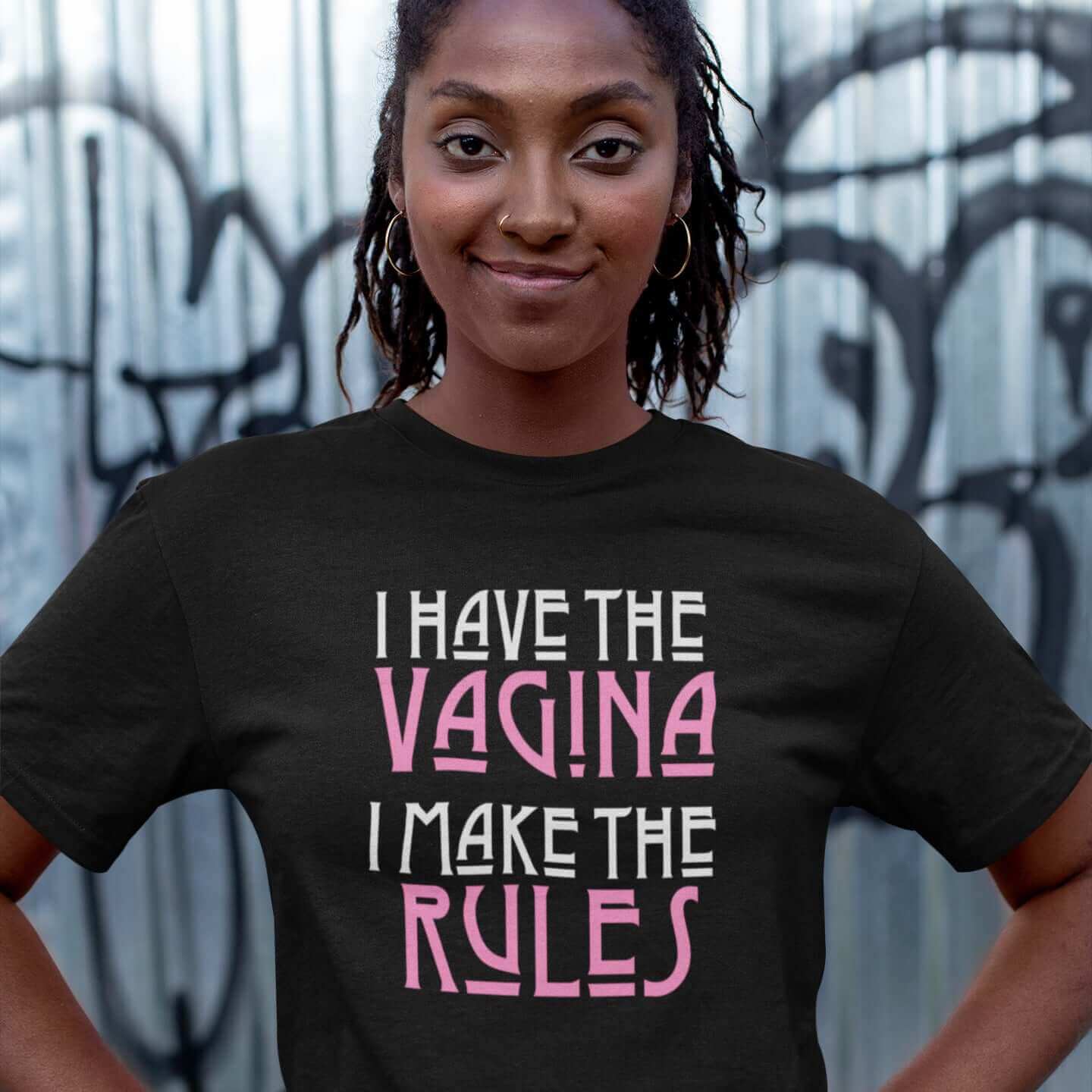 Woman wearing black t-shirt with the words I have the vagina , I make the rules printed on the front. The words vagina and rules are pink, the rest of the words are white.