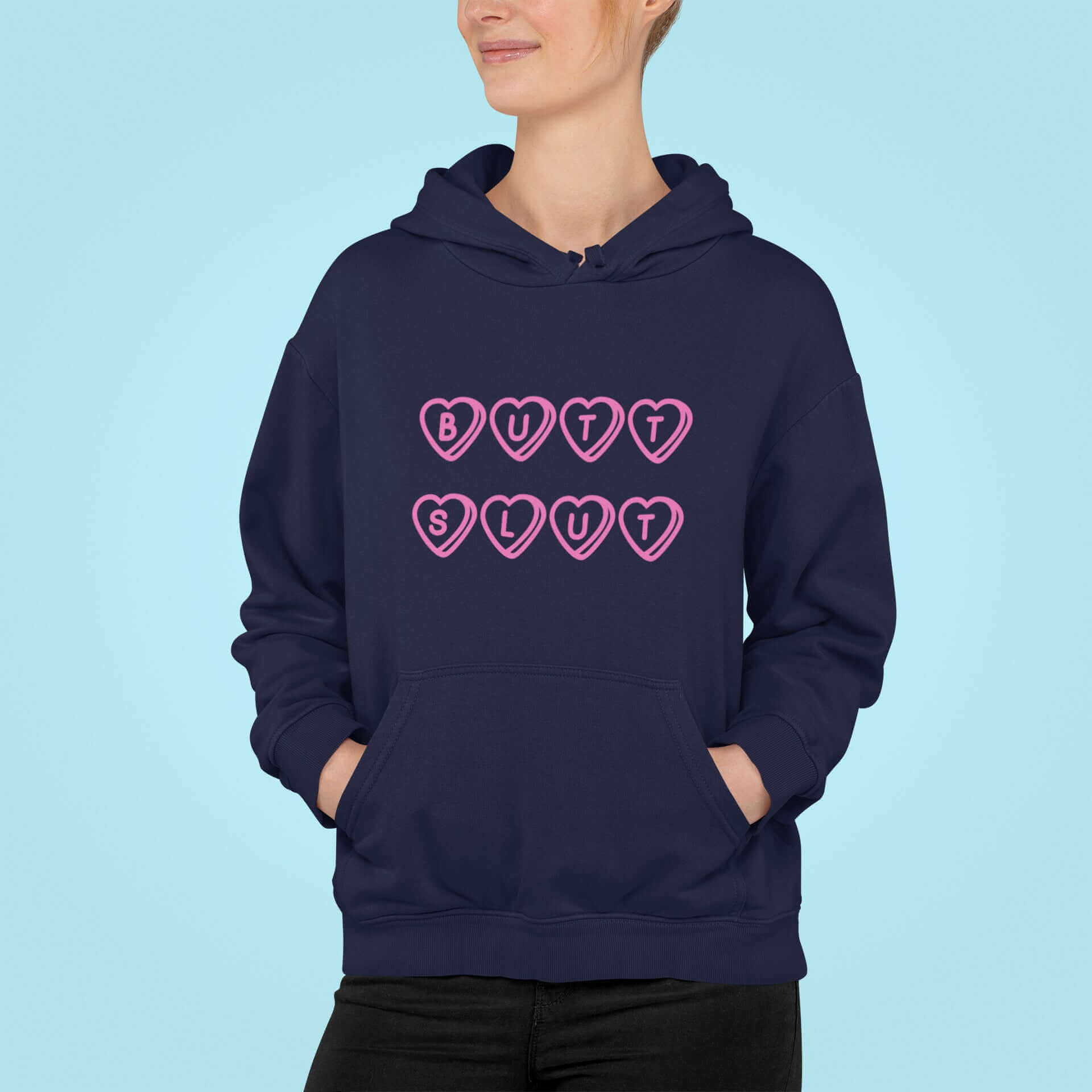 Woman wearing navy blue hoodie sweatshirt with the words Butt Slut printed in pink on the front. Pink hearts are around each letter in the text.