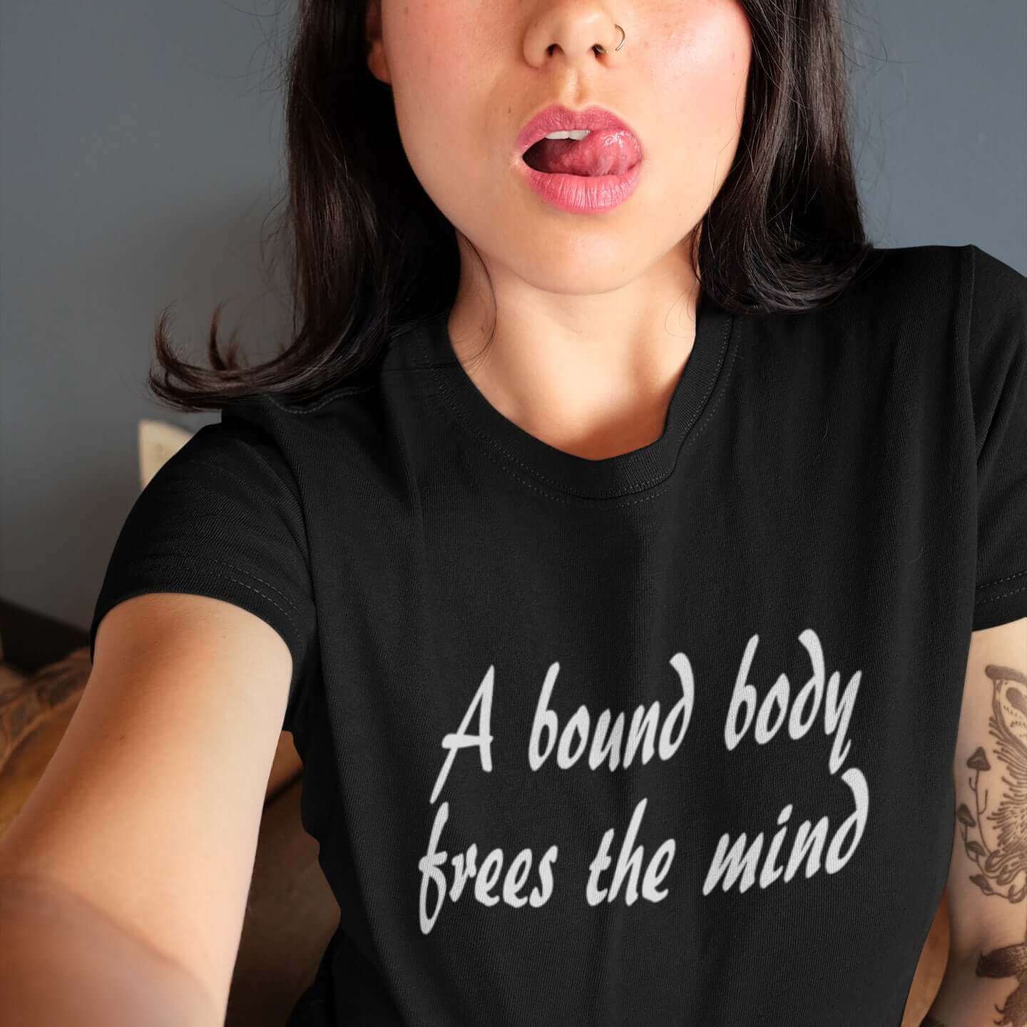 Woman wearing a black t-shirt with the BDSM phrase A bound body frees the mind printed on the front.