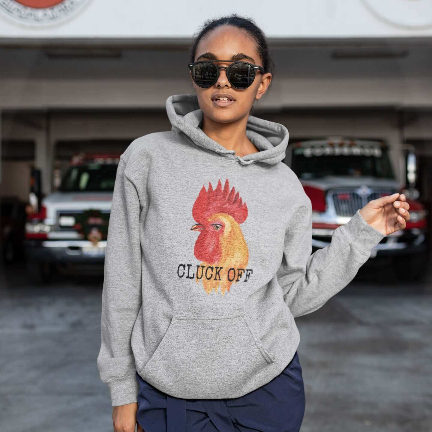 Woman wearing light sport grey hoodie sweatshirt that has graphic of a chicken and the words Cluck off printed on the front.