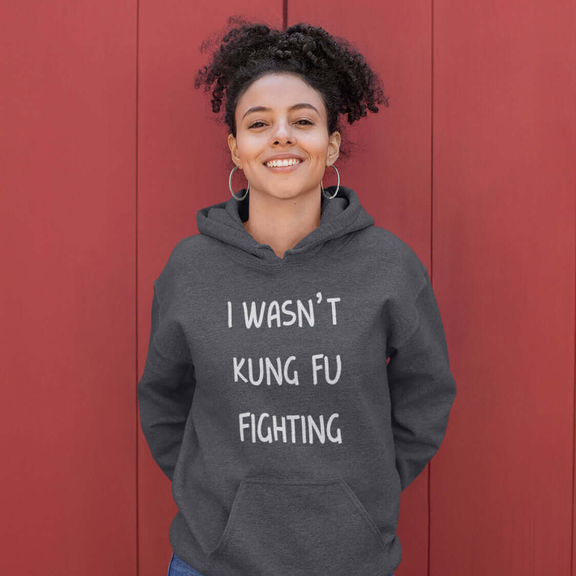 Grinning woman wearing dark grey hoodie sweatshirt with the funny phrase I wasn't kung fu fighting printed on the front.