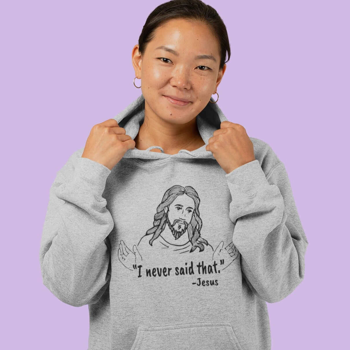 Woman wearing light grey hoodie sweatshirt. The hoodie has a line drawing of Jesus with his hands outstretched and the quote I never said that printed on the front.