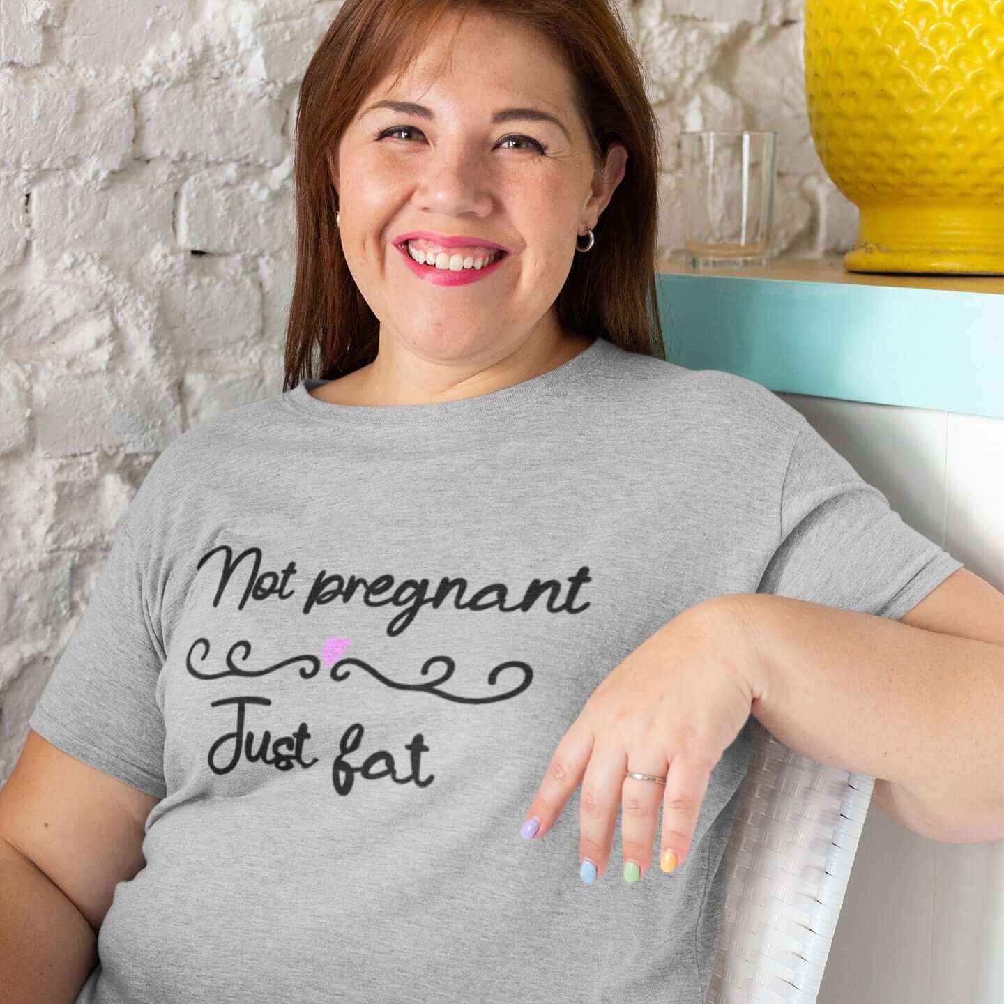 Smiling woman wearing a grey t-shirt with the words Not pregnant just fat printed on the front with a heart.