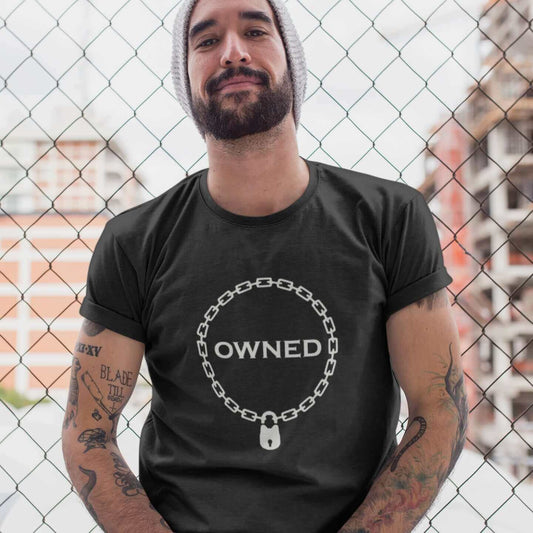 Man wearing a black t-shirt with an image of a BDSM chain collar with a lock and the word Owned printed in the center of the collar. The design is printed on the front of the shirt.