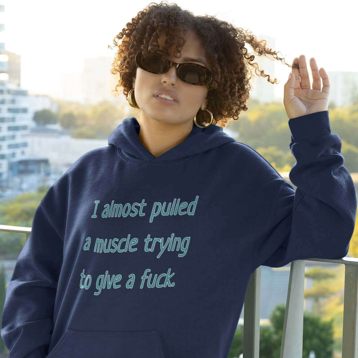 Woman wearing navy blue hooded sweatshirt with the words I Almost pulled a muscle trying to give a fuck printed on the front.