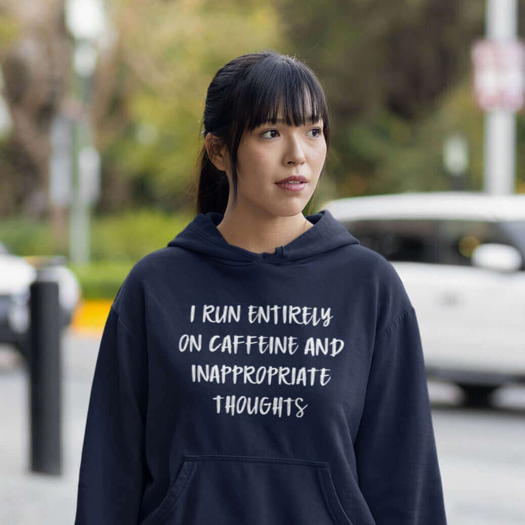 Woman wearing navy blue hoodie sweatshirt with the words I run entirely on caffeine & inappropriate thoughts printed on the front.