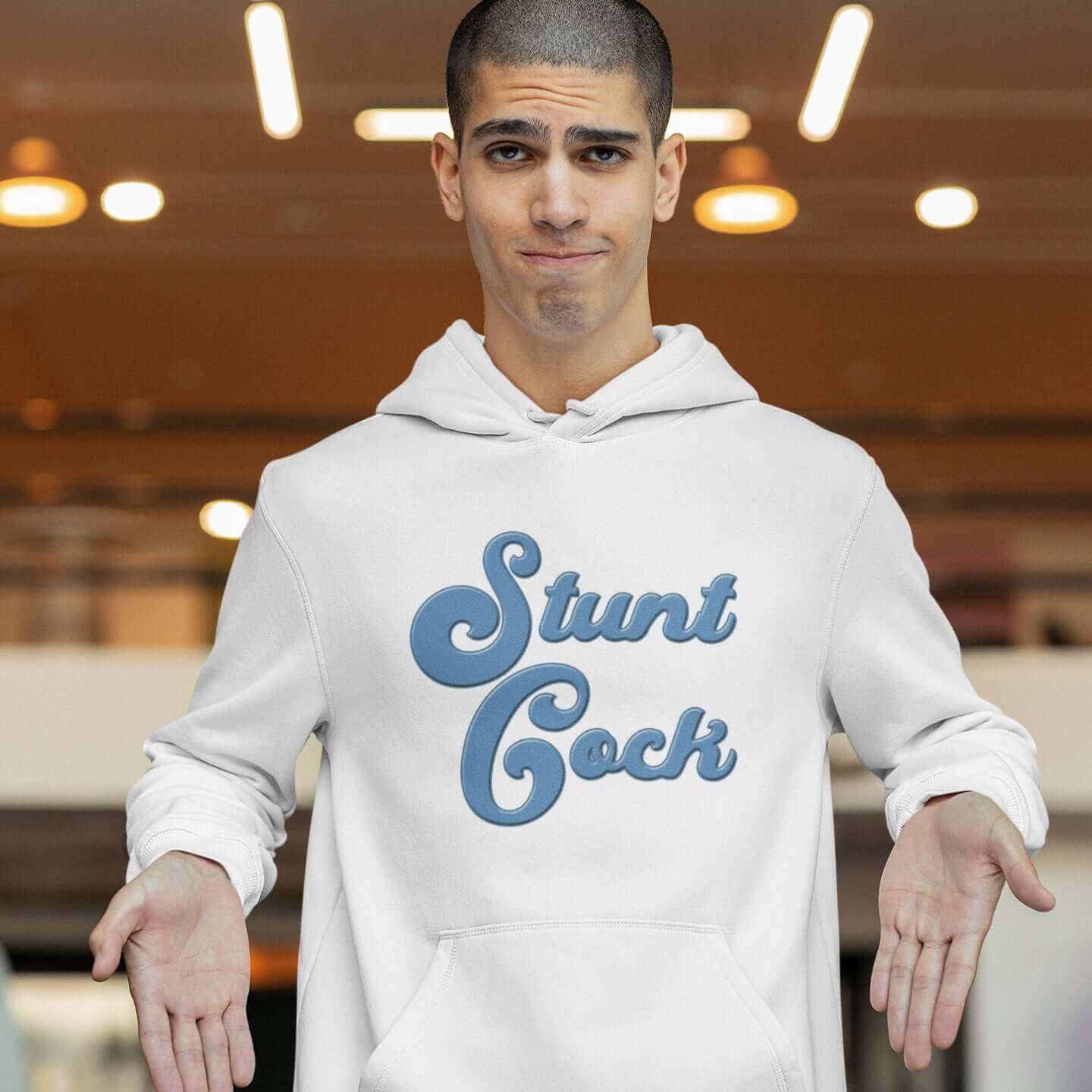 Man making funny face gesturing to the front of his hoodie. He is wearing a white hooded sweatshirt with the words Stunt Cock printed on the front in blue.