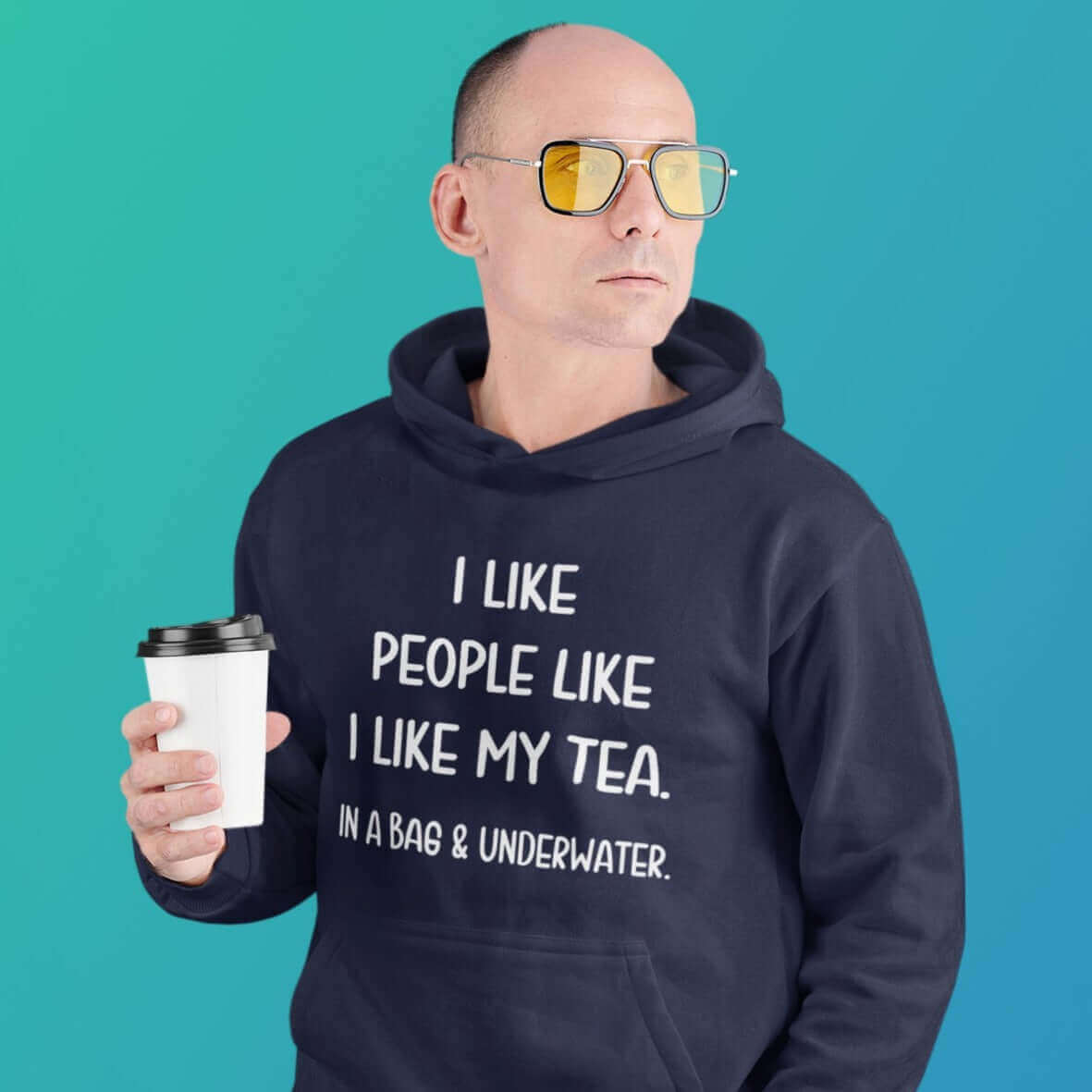 Serious looking man holding cup of tea. He is wearing a navy blue hoodie sweatshirt with the phrase I like people like I like my tea, In a bag & underwater printed on the front.