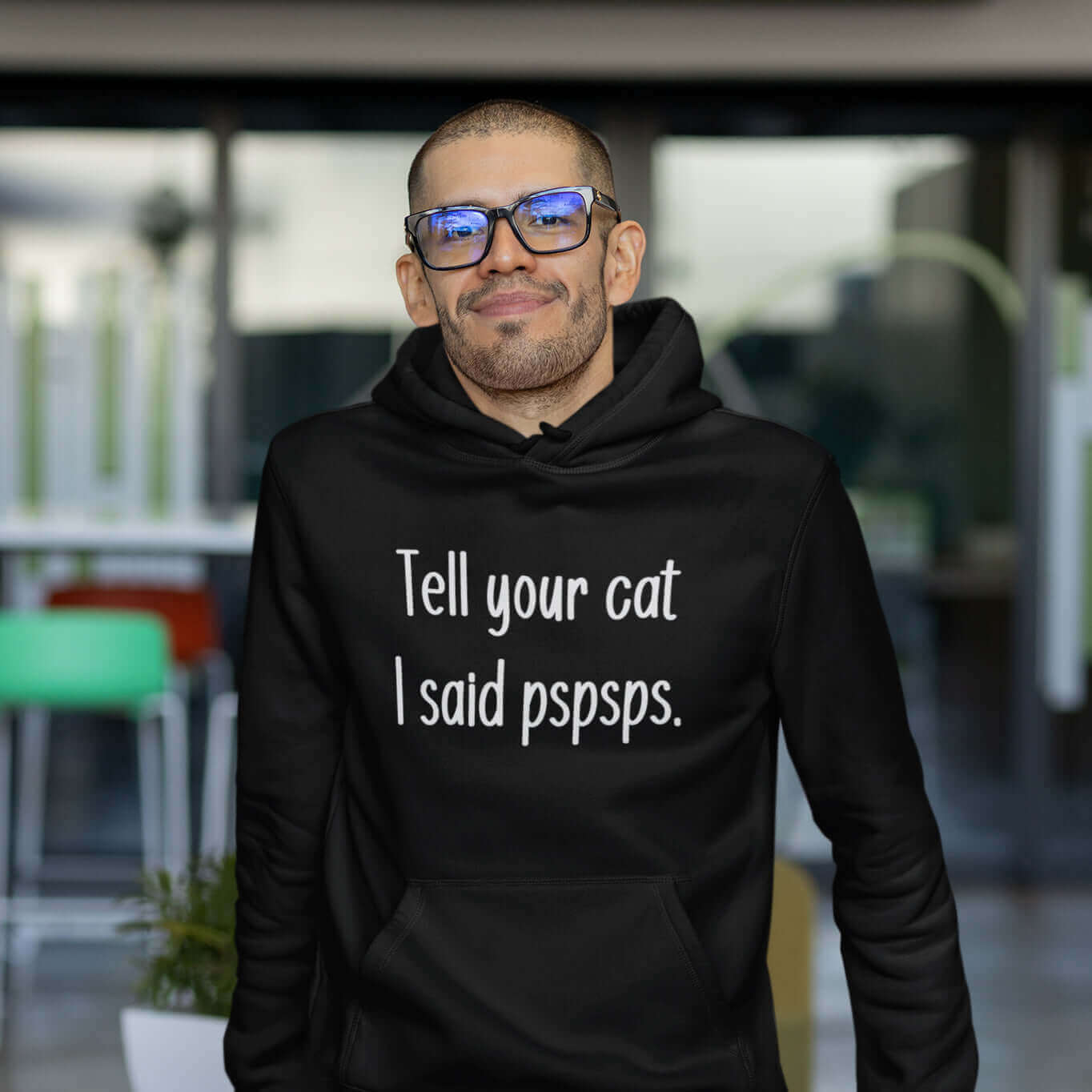 Man wearing black hooded sweatshirt with the words Tell your cat I said pspsps printed on the front.