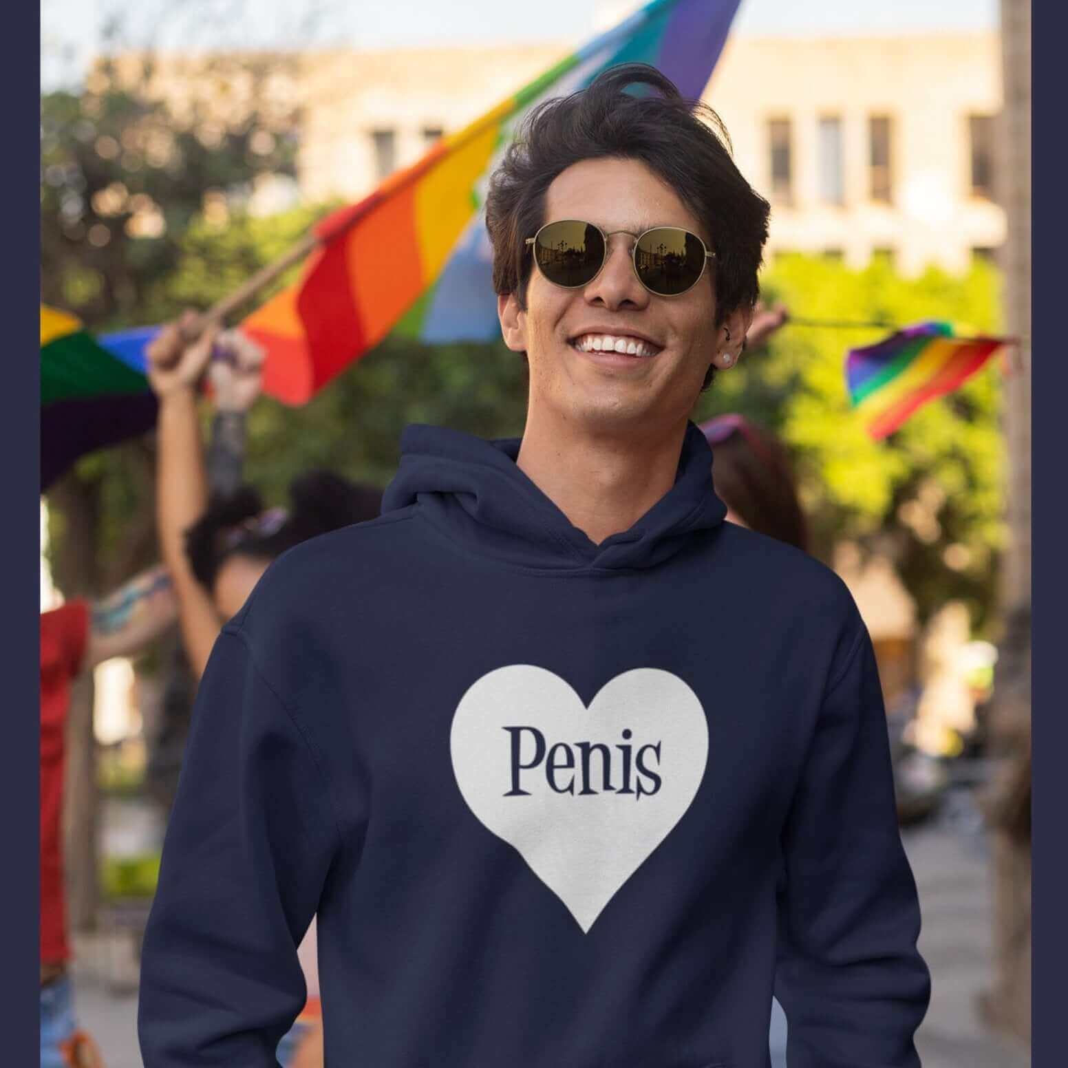 Man at a pride event wearing a navy blue hoodie sweatshirt with a heart image printed on the front. The word penis is inside the heart