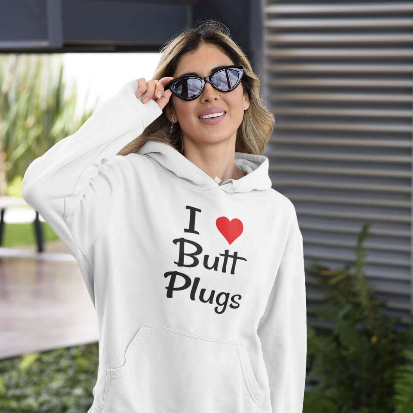 Woman wearing sunglasses and white hooded sweatshirt with I heart butt plugs printed on the front.