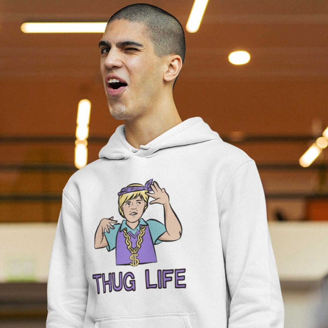 Man laughing wearing a white hoodie sweatshirt with a parody image of a blond haired child trying to be a gangster with the words Thug Life printed on the front.