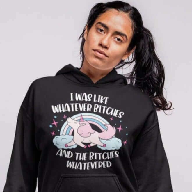 Woman wearing a black hoodie sweatshirt with a prancing unicorn rainbow graphic. The phrase I was like whatever bitches and the bitches whatevered printed on the front.