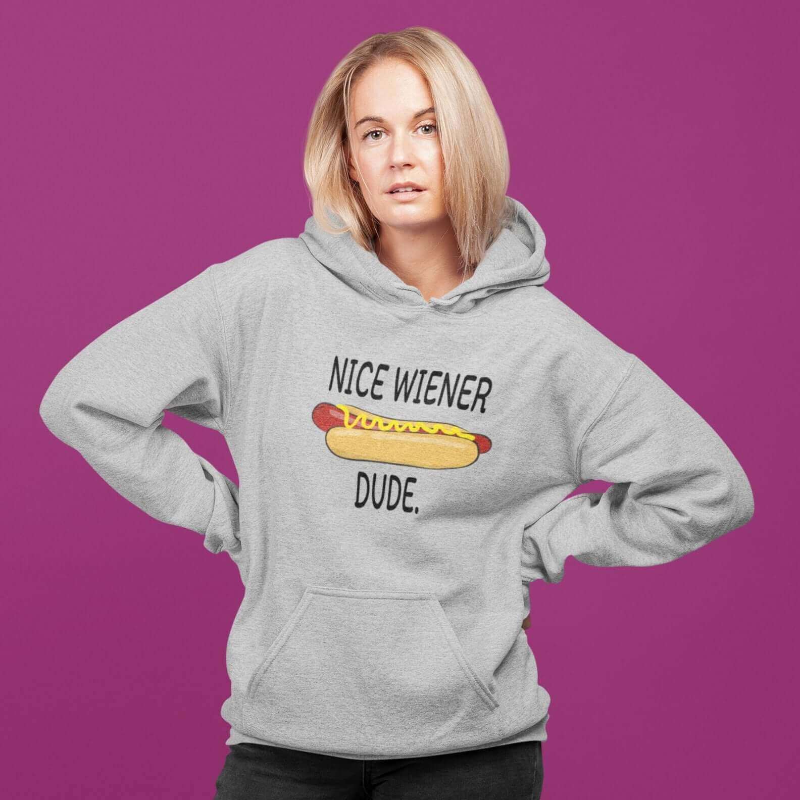 Woman wearing a light grey hoodie sweatshirt with an image of a hotdog and the phrase Nice wiener dude printed on the front.