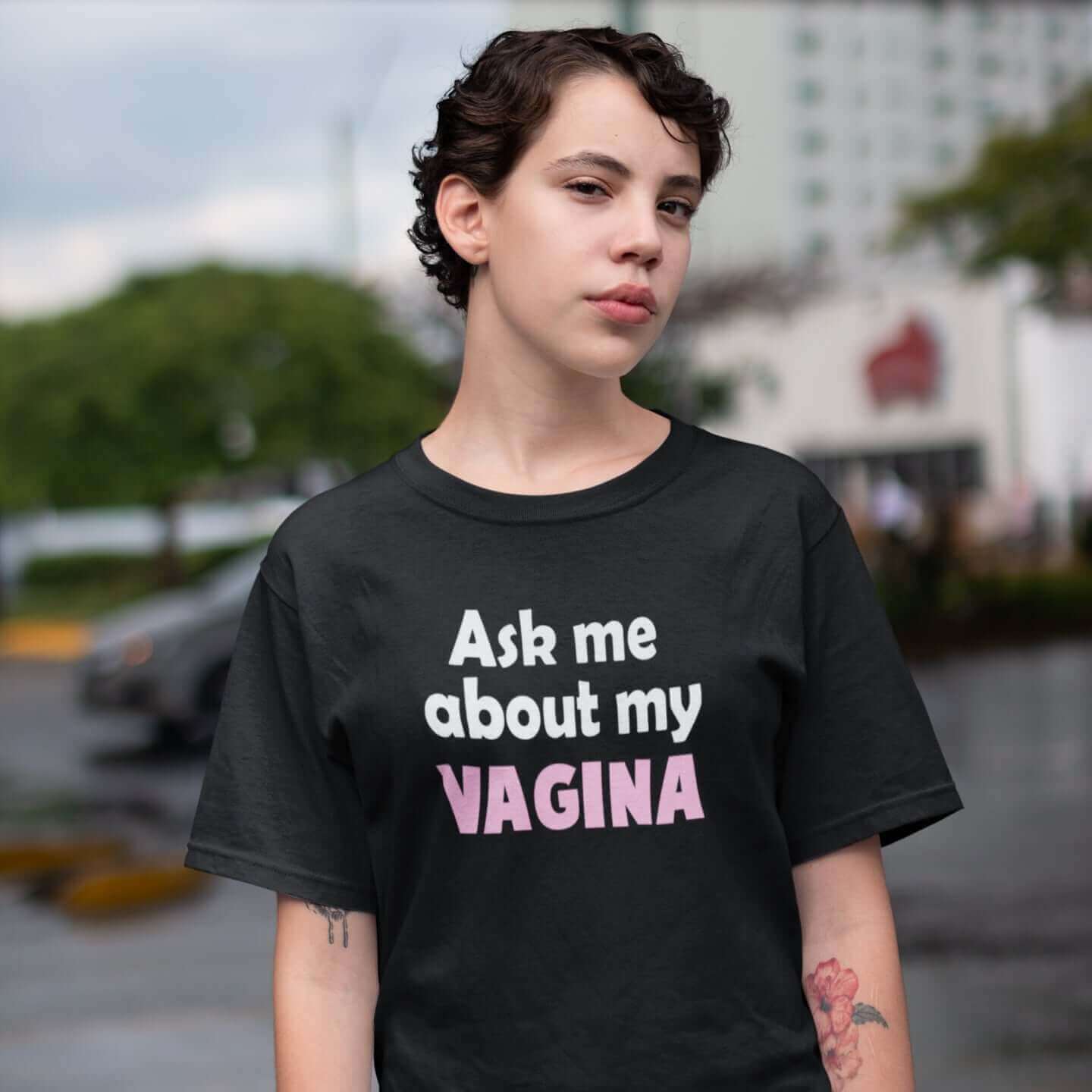 Woman wearing black t-shirt with the words Ask me about my vagina printed on the front. The word vagina is printed in pink. The rest of the text is white..