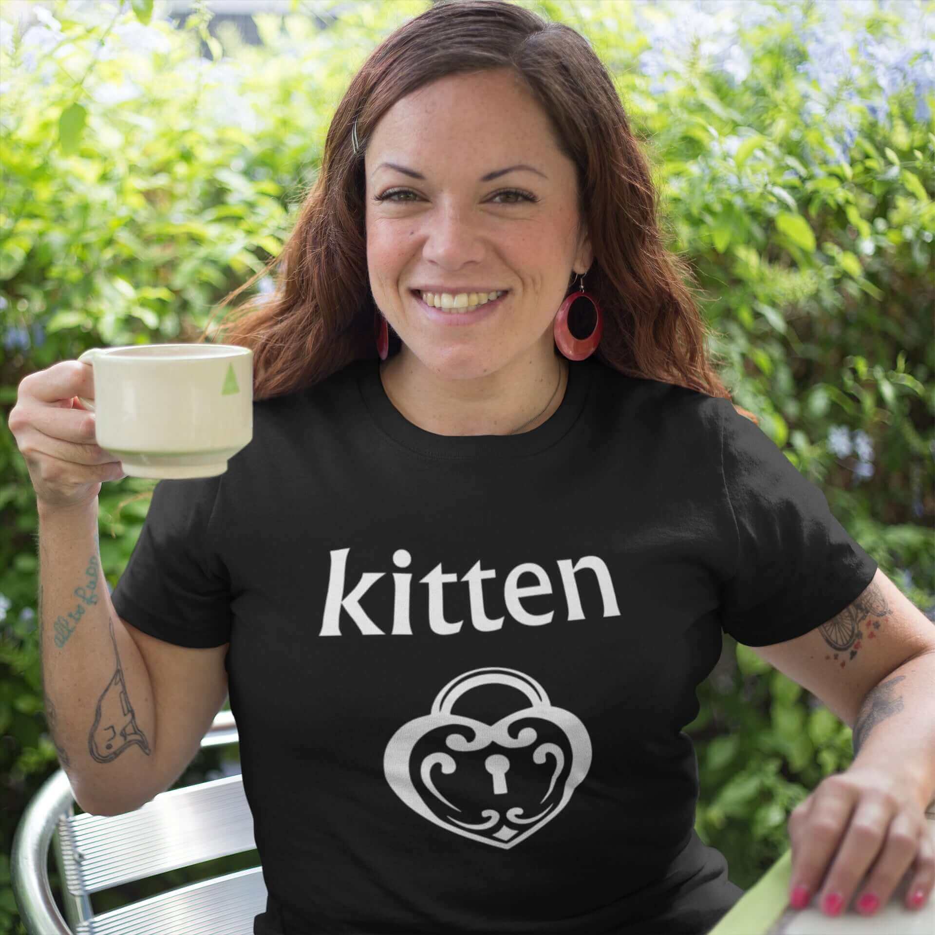 Woman wearing a black t-shirt with an image of a BDSM heart shaped lock and the word kitten printed on the front.