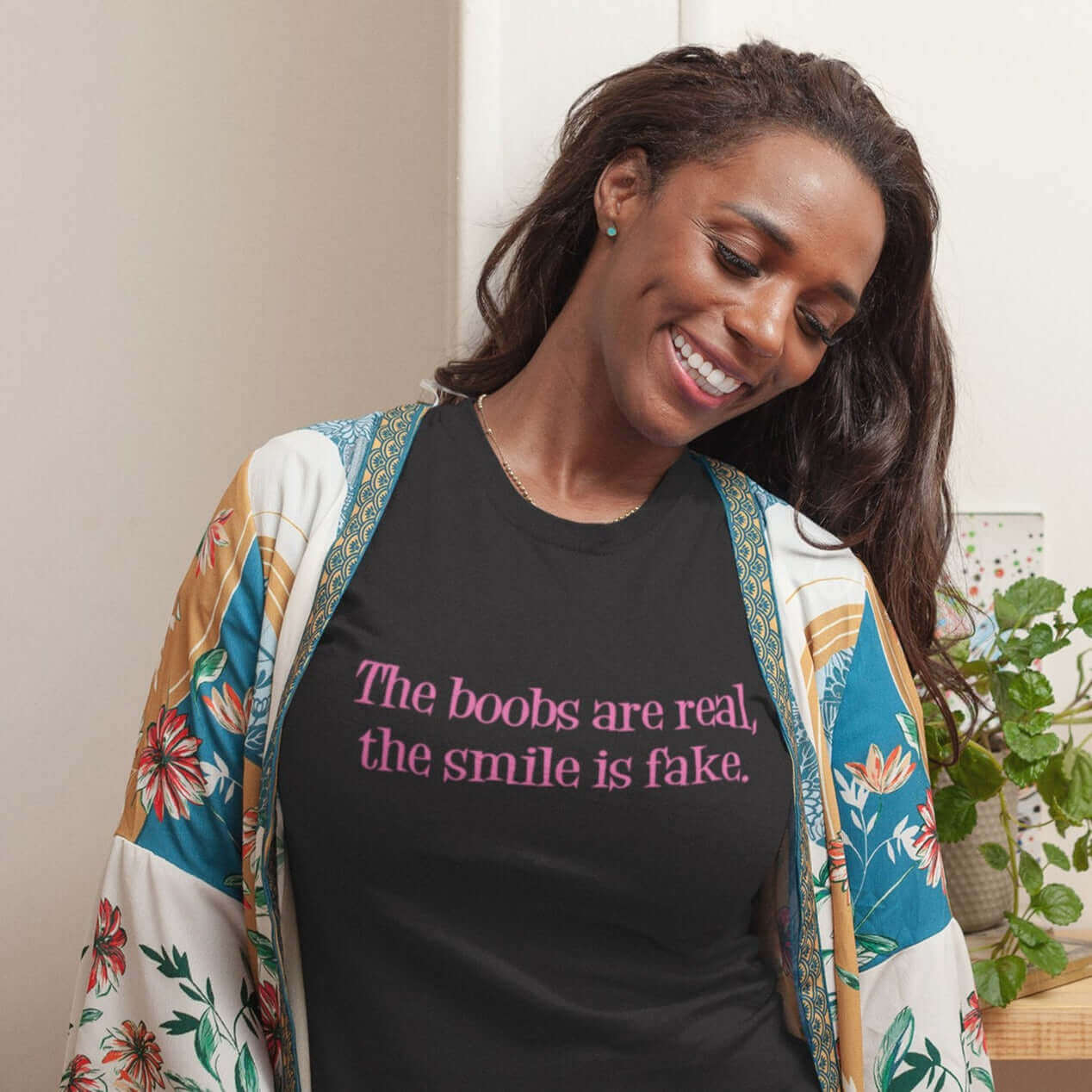Smiling woman wearing a black t-shirt with the phrase The boobs are real, the smile is fake printed in pink on the front.