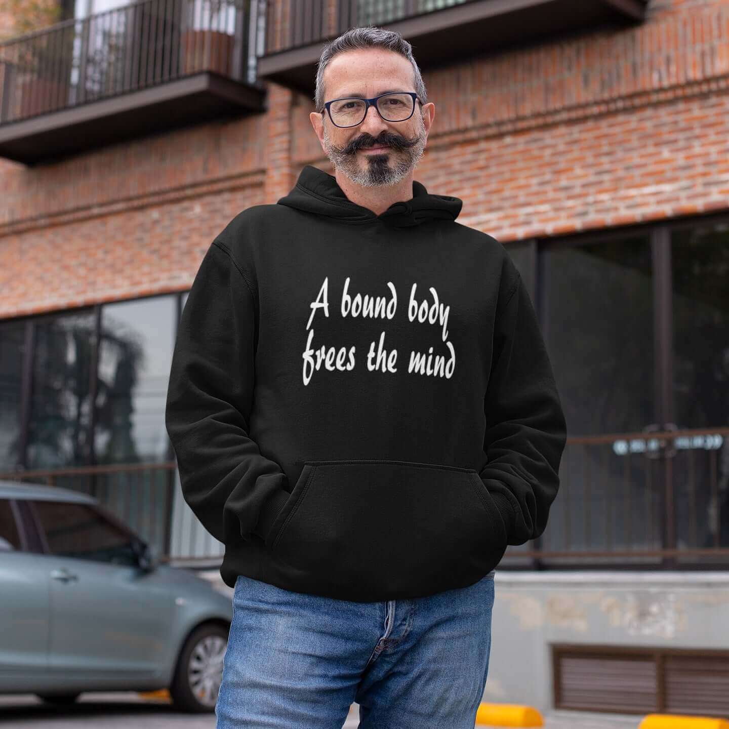 Man wearing a black hoodie sweatshirt with the BDSM phrase A bound body frees the mind printed on the front.