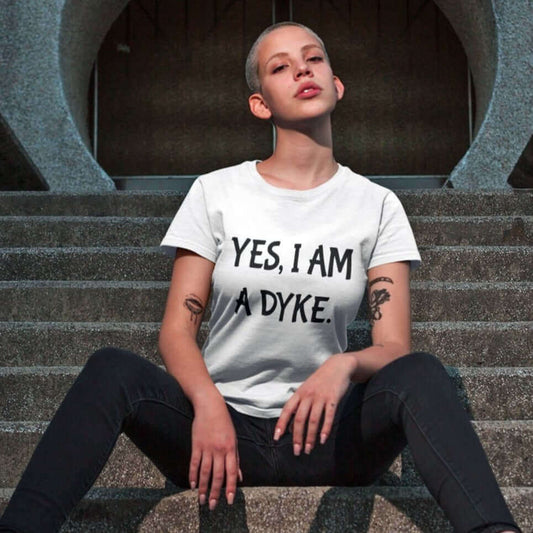 Woman with short hair wearing white t-shirt with the words Yes, I'm a dyke printed on the front.