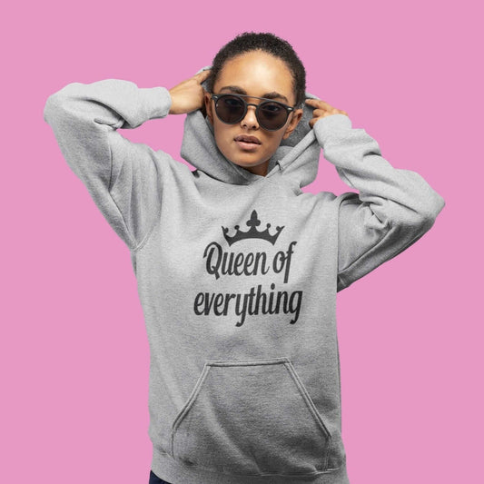 Woman wearing sunglasses and a light grey hoodie sweatshirt. The hoodie has an image of a crown and the phrase Queen of everything printed on the front.