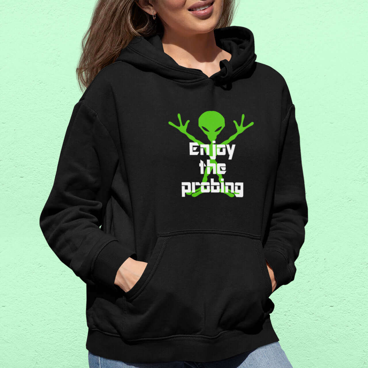 Woman wearing a black hoodie sweatshirt with an image of an alien and the funny phrase Enjoy the probing printed on the front.