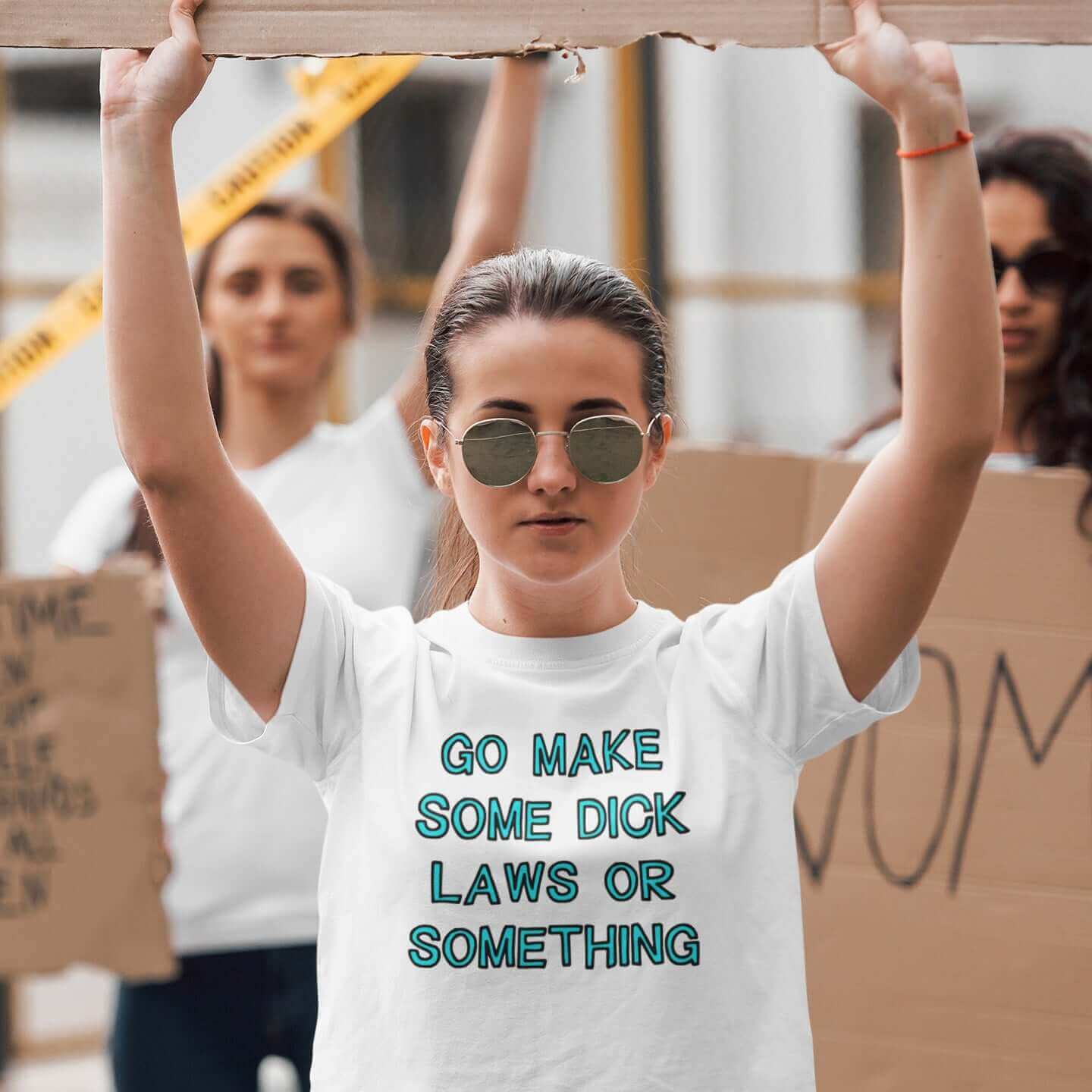 Woman at a protest wearing a white t-shirt with the words Go make some dick laws or something printed on the front. The text is turquoise with black outline.