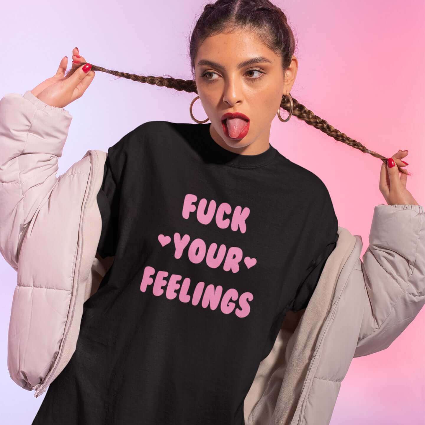 Woman wearing black t-shirt with the words Fuck your feelings printed on the front in pink. There are cute pink hearts next to the words.