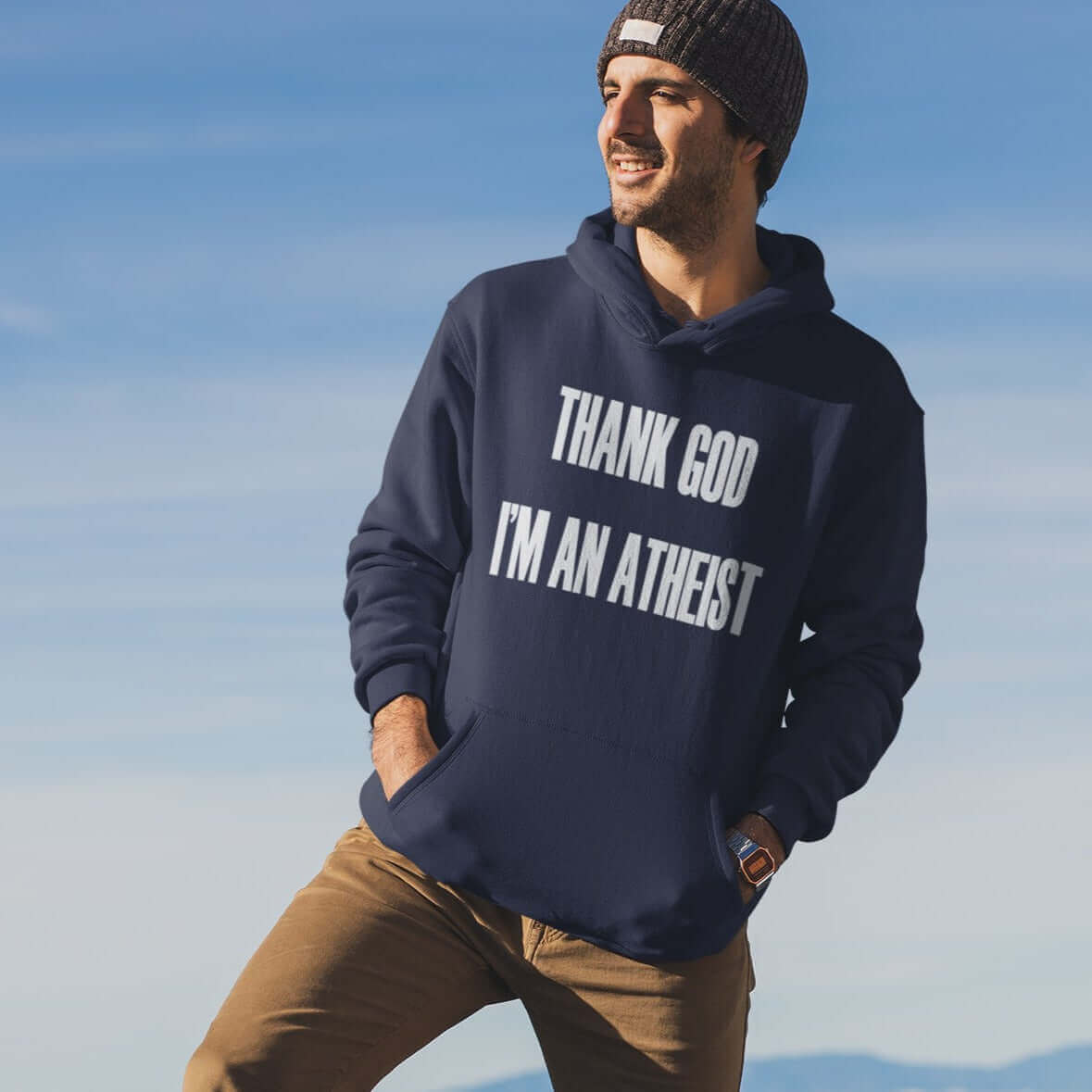 Man on top of a mountain wearing a navy blue hoodie sweatshirt with Thank God I'm an atheist printed on the front.