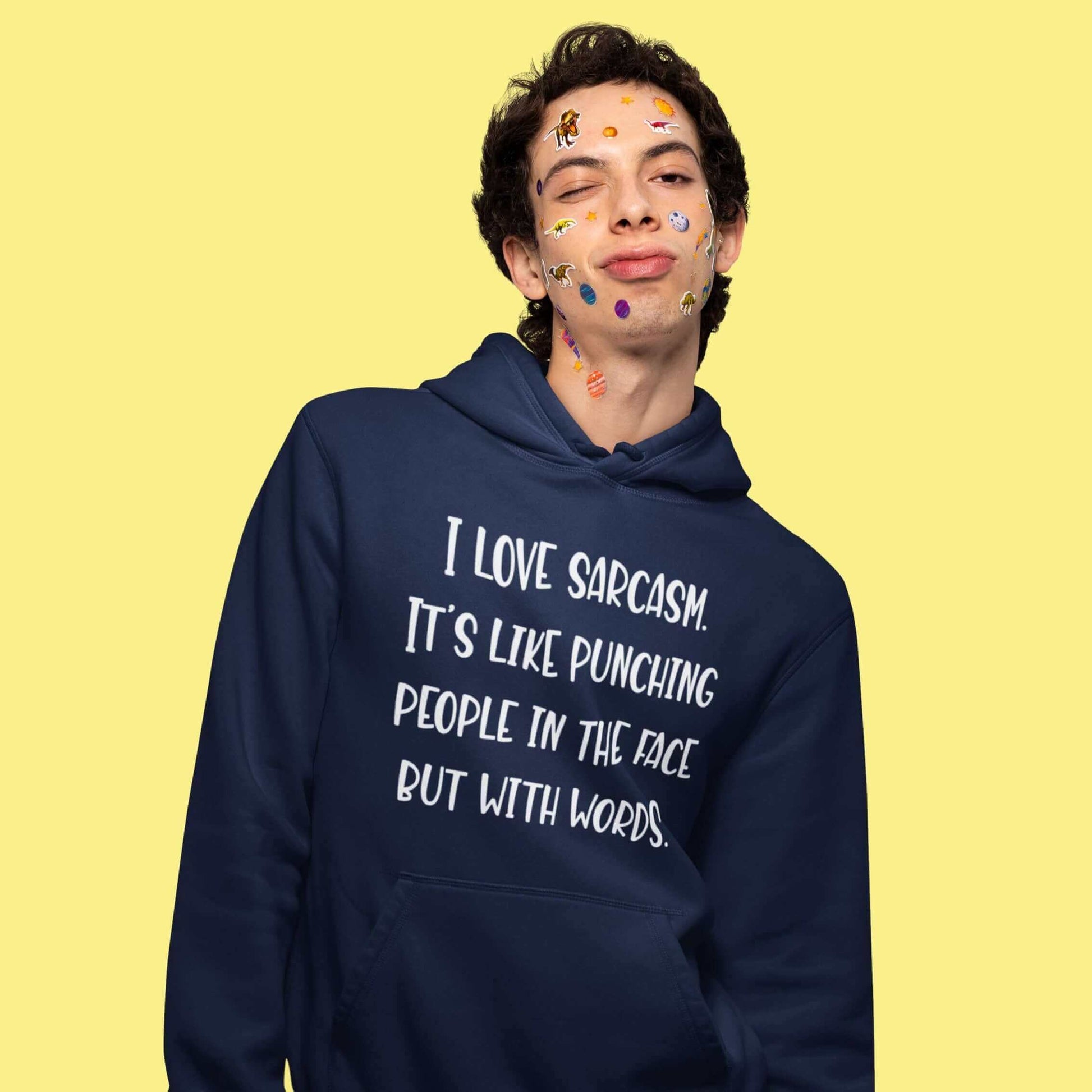 Man wearing a navy blue hoodie sweatshirt with the phrase I love sarcasm, it's like punching people in the face but with words printed on the front.