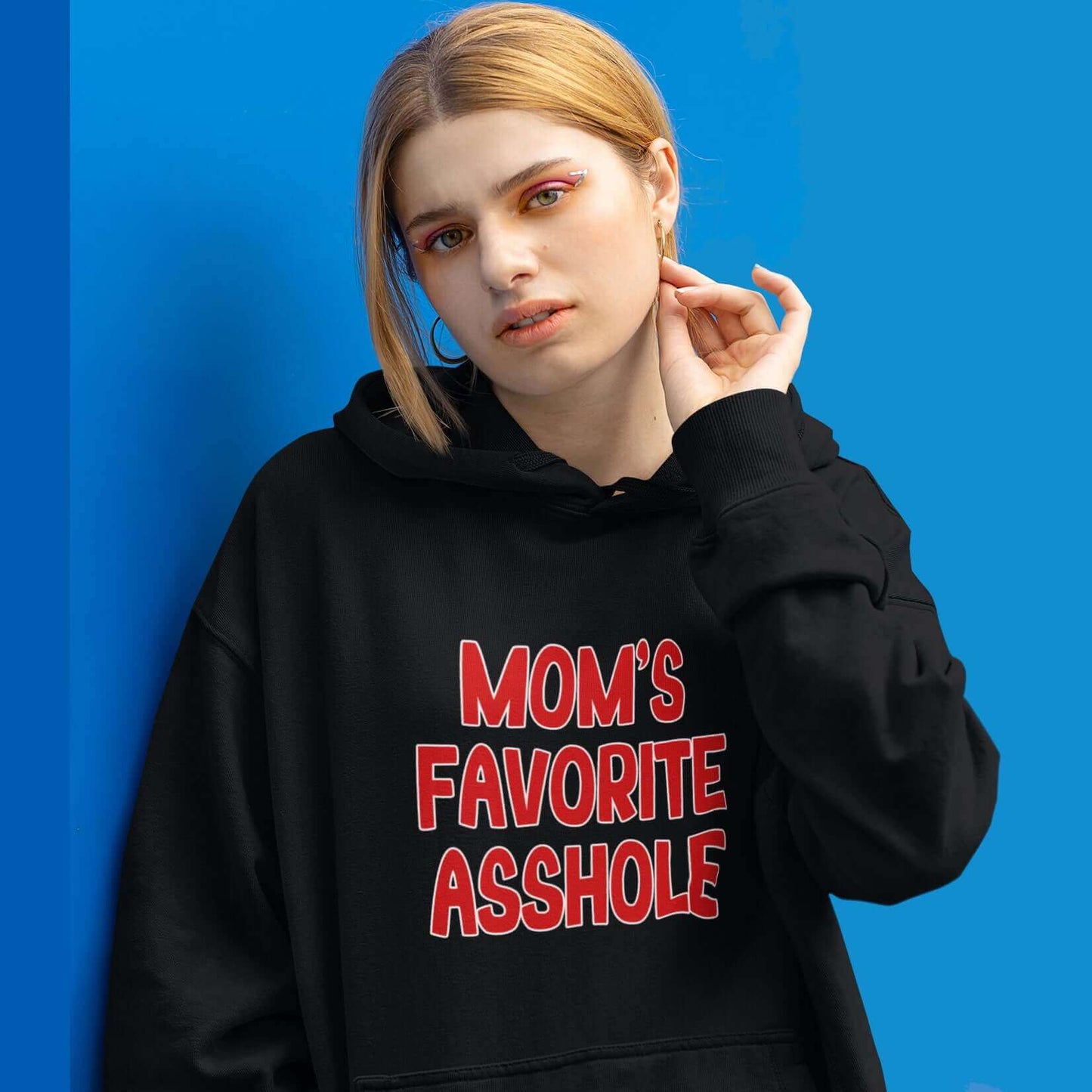 Woman wearing black hooded sweatshirt with the words Mom's favorite asshole printed in red on the front. 